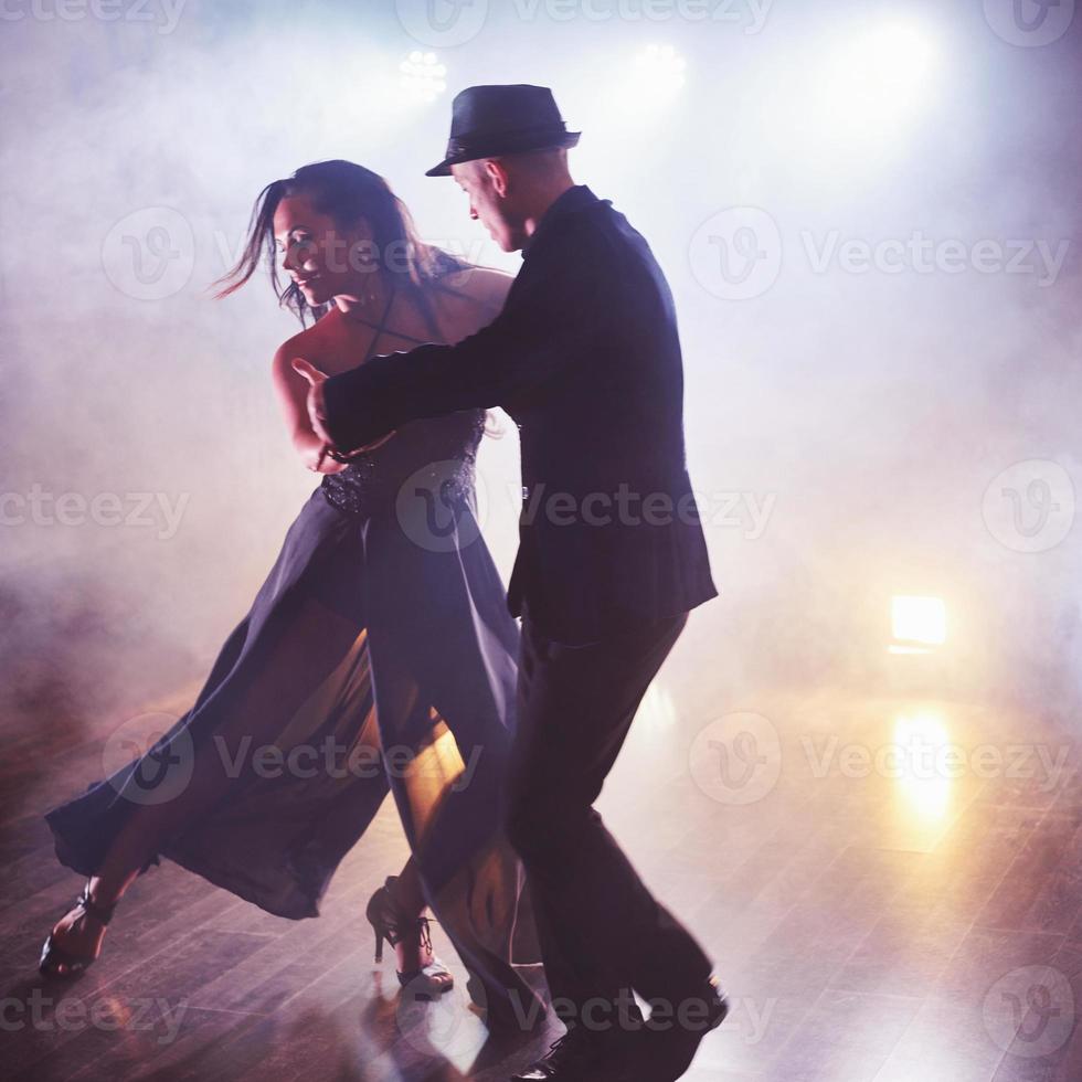dançarinos habilidosos se apresentando no quarto escuro sob a luz e a fumaça do show. casal sensual realizando uma dança contemporânea artística e emocional foto