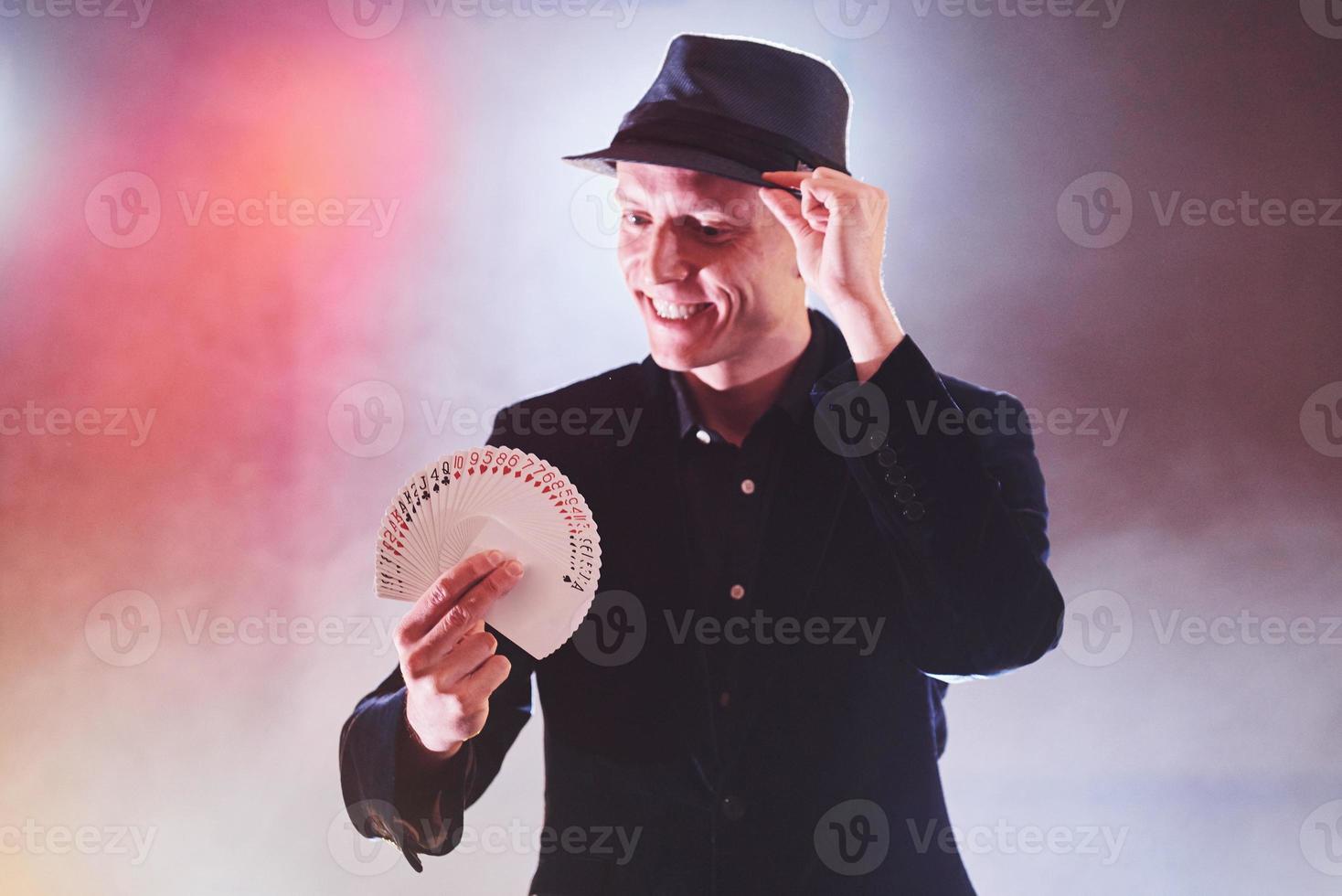 mágico mostrando truque com cartas de baralho. magia ou destreza, circo, jogo. prestidigitador em quarto escuro com neblina foto