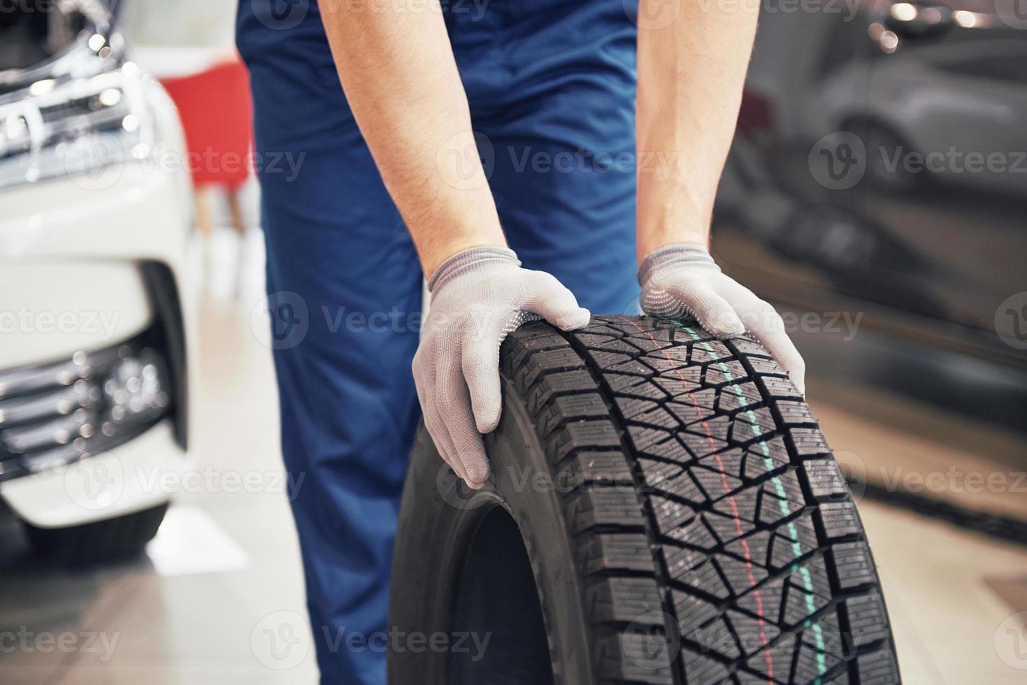 closeup de mãos de mecânico empurrando um pneu preto na oficina foto