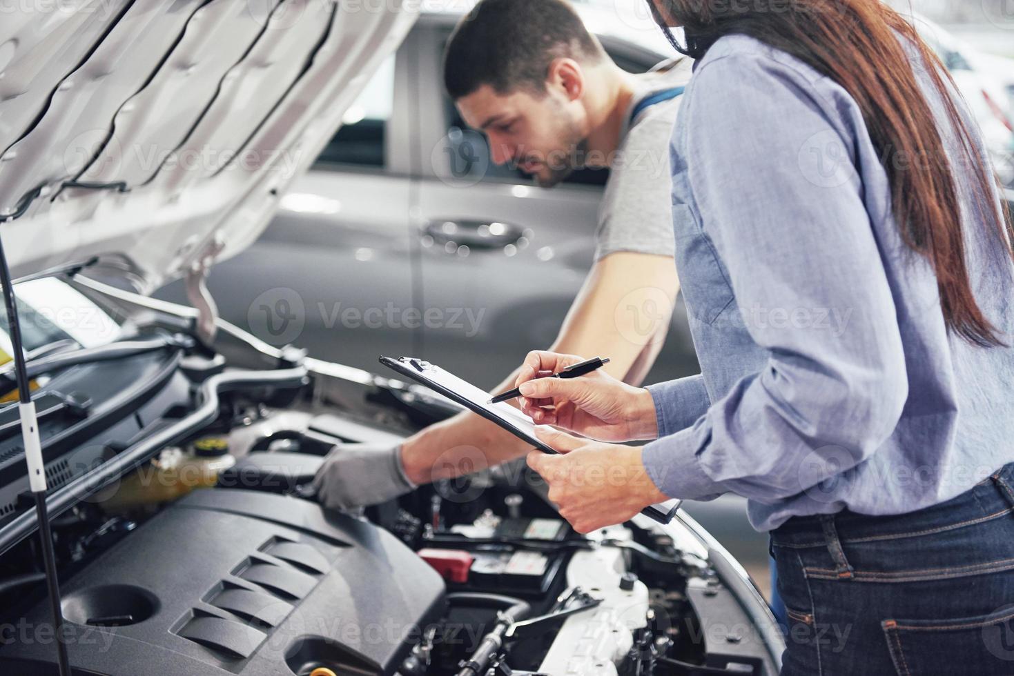 um homem mecânico e uma mulher cliente olham para o capô do carro e discutem reparos foto