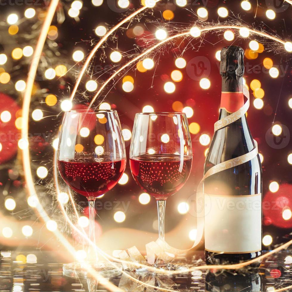 dois copos de vinho e garrafa de vinho tinto contra um fundo escuro com luz dourada cintilante e bokeh foto