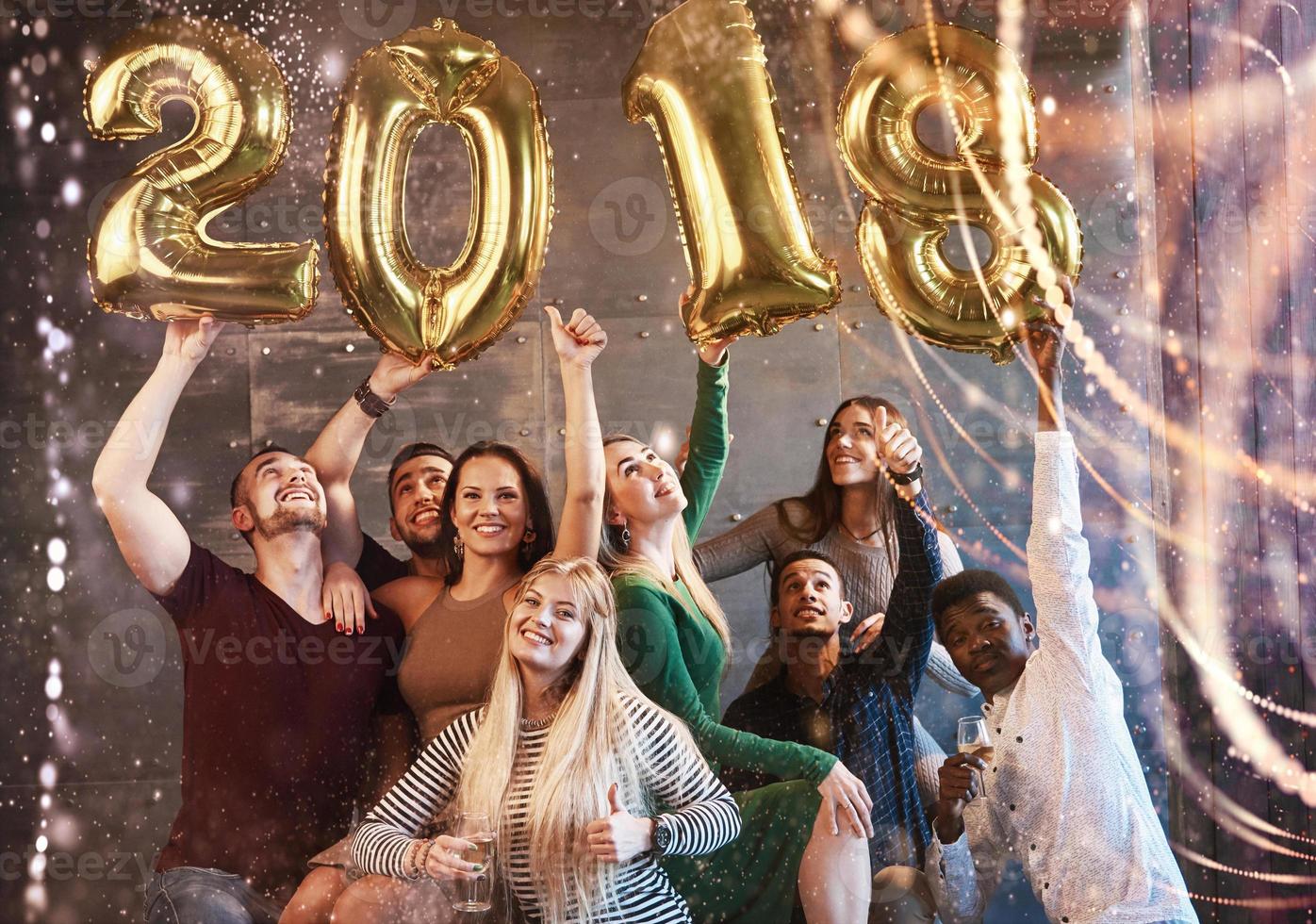 um grupo de jovens alegres segura números que indicam a chegada de um novo ano de 2018. a festa é dedicada à celebração do ano novo. conceitos sobre estilo de vida de união da juventude foto