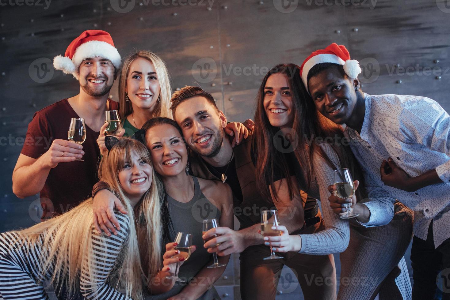 grupo de jovens lindos fazendo selfie na festa de ano novo, melhores amigos, meninas e meninos juntos, se divertindo, posando de pessoas de estilo de vida emocional. chapéus de Papai Noel e taças de champanhe nas mãos foto