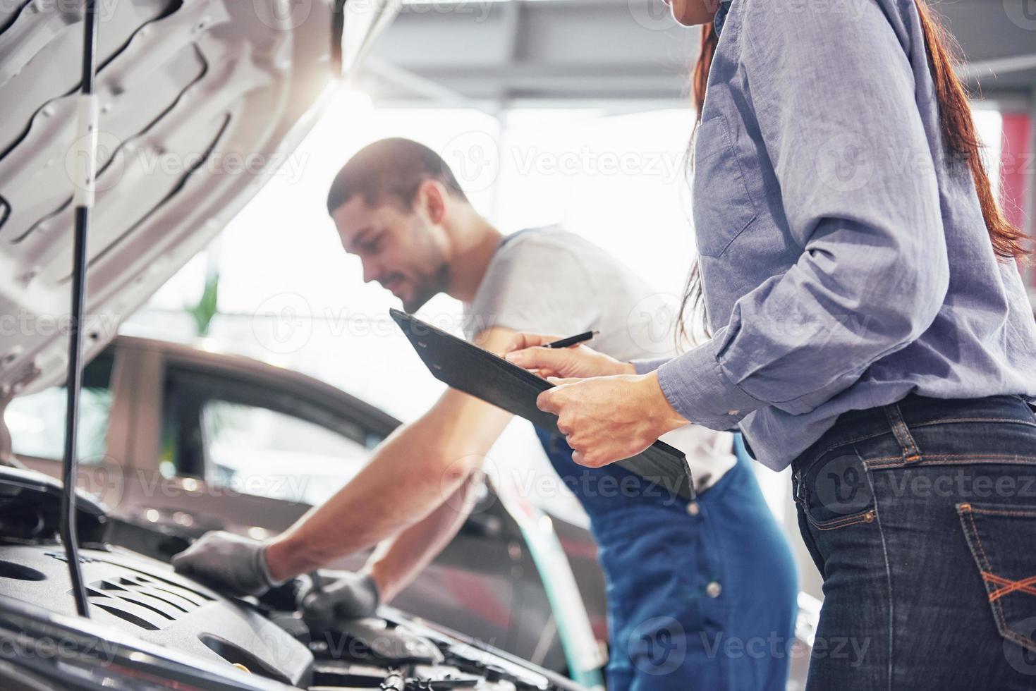 um homem mecânico e uma mulher cliente olham para o capô do carro e discutem reparos foto