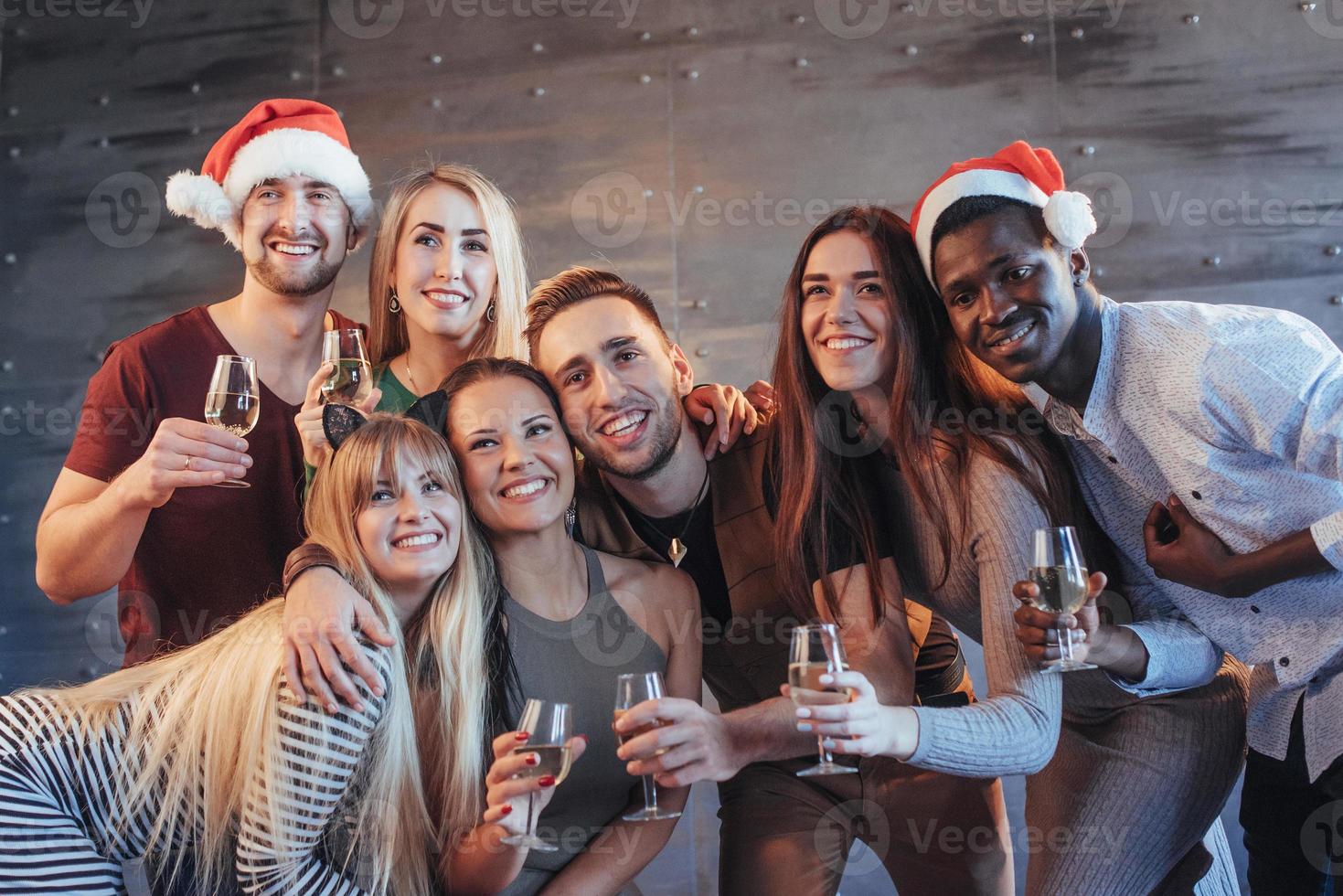 grupo de jovens lindos fazendo selfie na festa de ano novo, melhores amigos, meninas e meninos juntos, se divertindo, posando de pessoas de estilo de vida emocional. chapéus de Papai Noel e taças de champanhe nas mãos foto