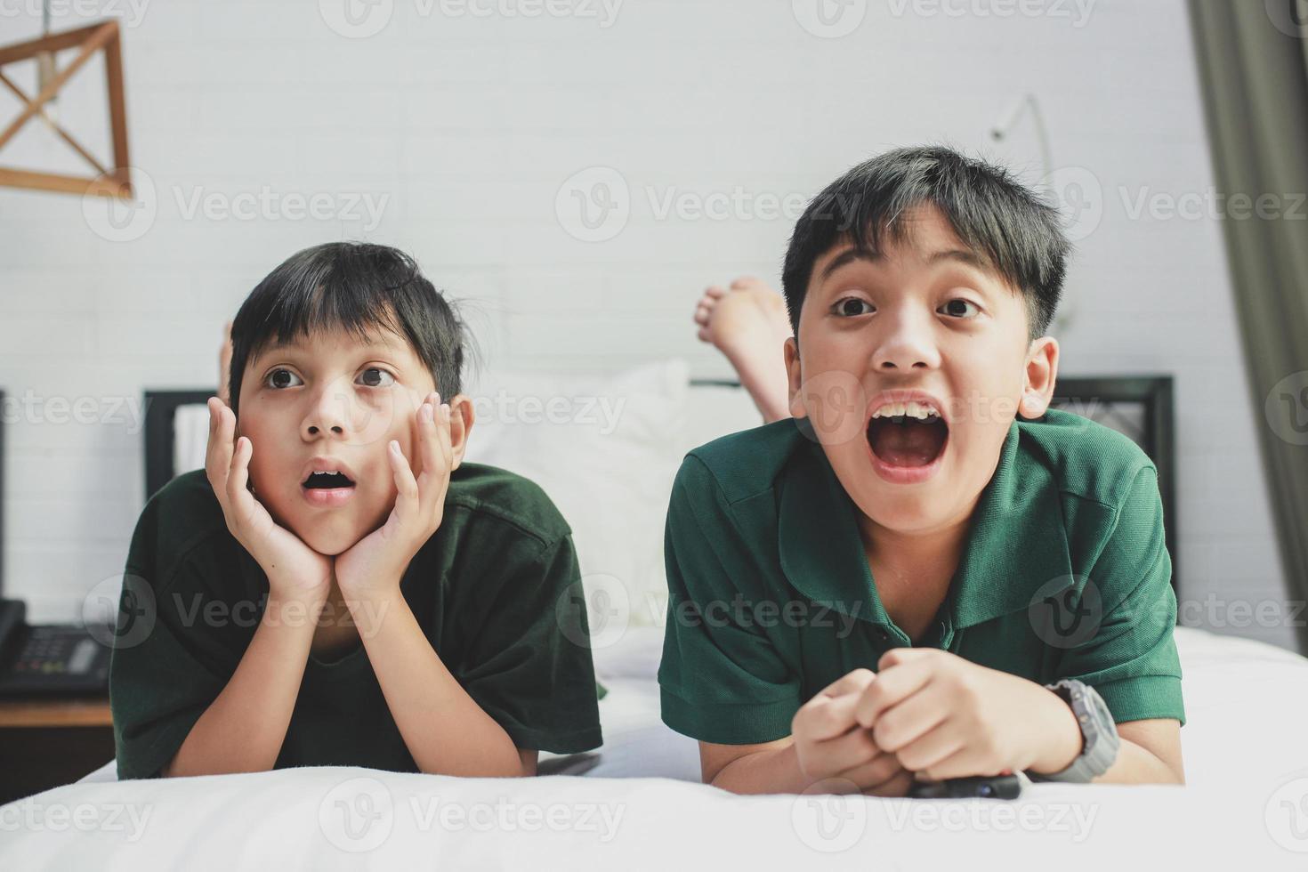 dois irmãos deitados na cama assistindo televisão com expressão de meia foto