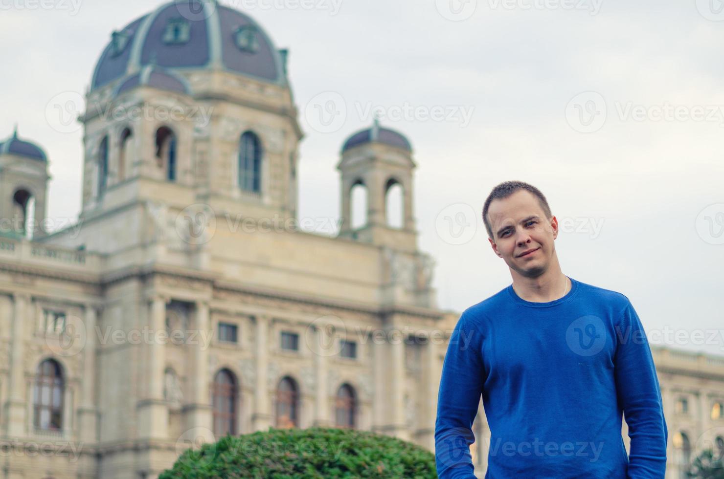 jovem viajante olhando para a câmera, sorrindo e posando, kunsthistorisches construindo na cidade de viena foto