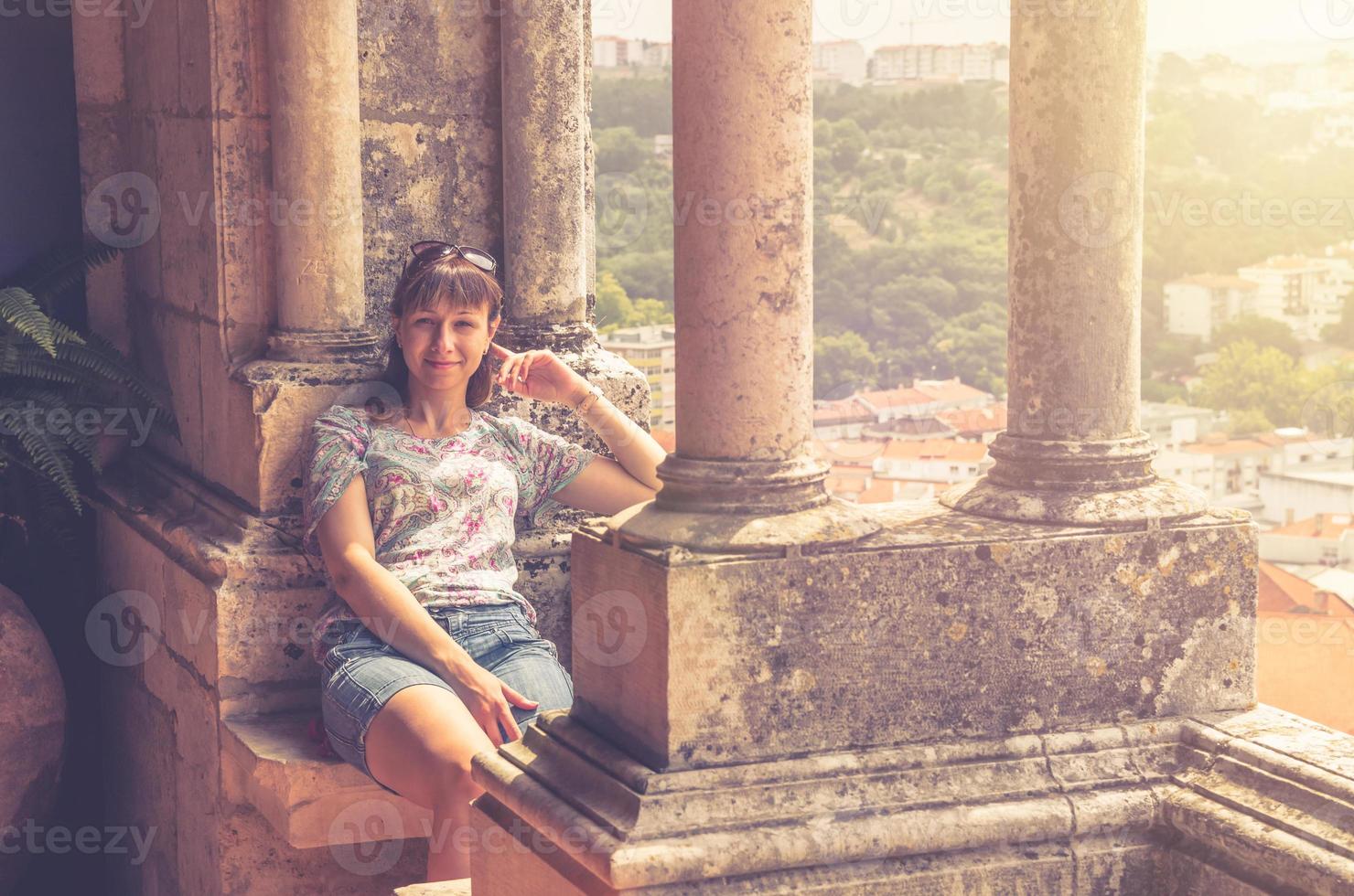 jovem viajante bonita olhando para a câmera, posando e sentado na varanda com colunas de pedra foto