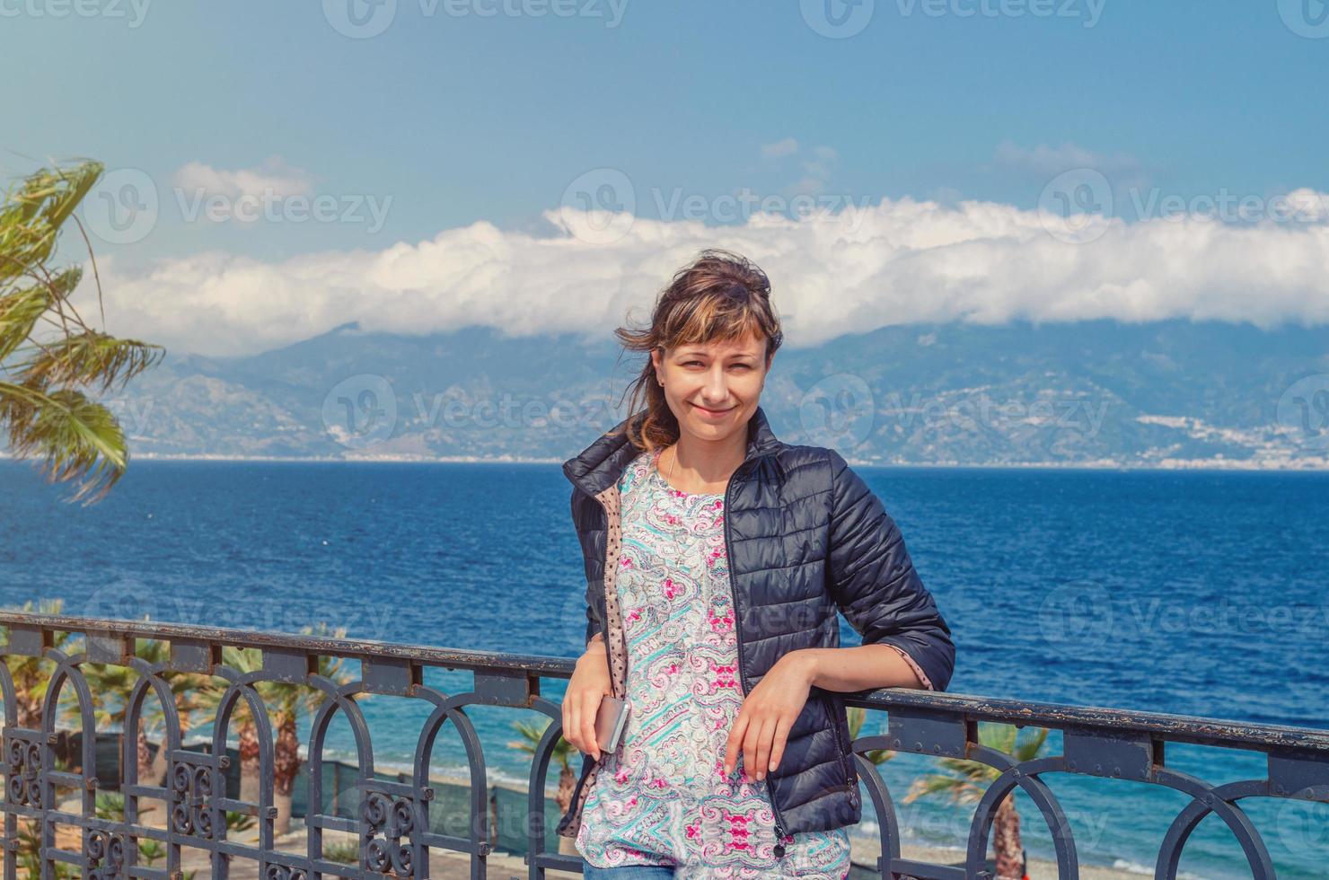 jovem e bela viajante olhando a câmera, sorrindo e posando no aterro lungomare falcomata em reggio calabria foto