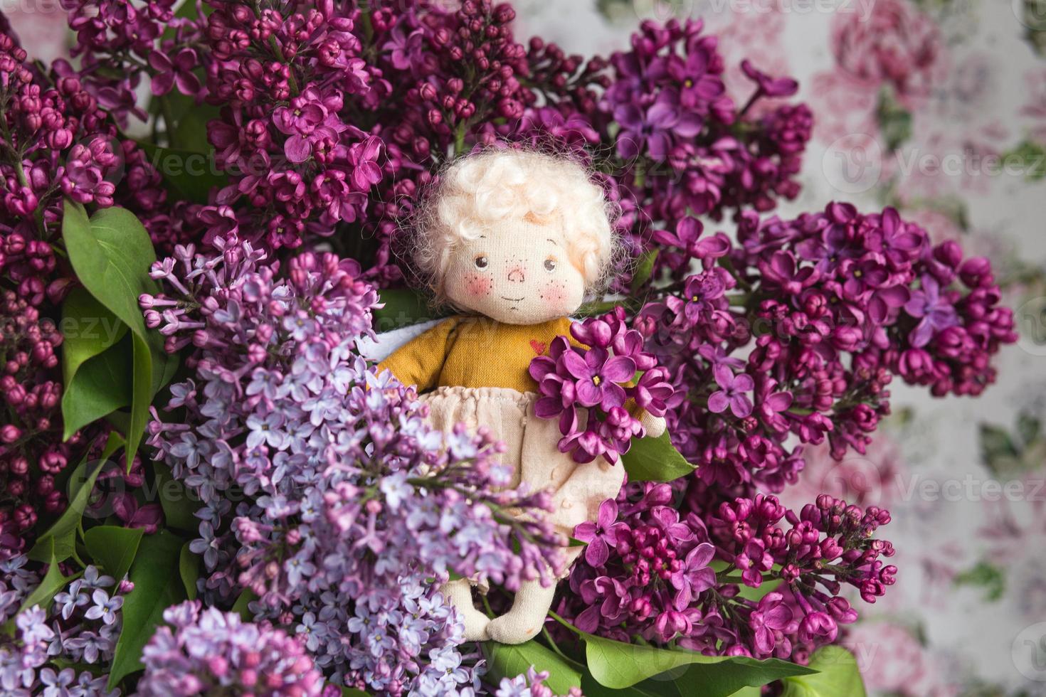 anjinho de cabelos dourados nas flores lilás azul, rosa, roxo, violeta. brinquedo artesanal em cores lilás violetas. cartão de saudação. foto