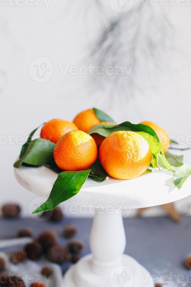 tangerinas laranja em fundo cinza na decoração de ano novo com pinhas marrons e folhas verdes. decoração de natal com tangerinas. deliciosa clementina doce. foto