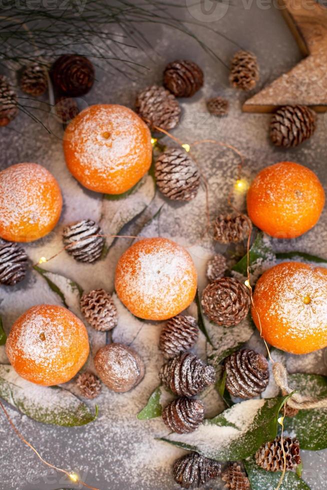 tangerinas laranja em fundo cinza na decoração de ano novo com pinhas marrons e folhas verdes. decoração de natal com tangerinas. deliciosa clementina doce. foto