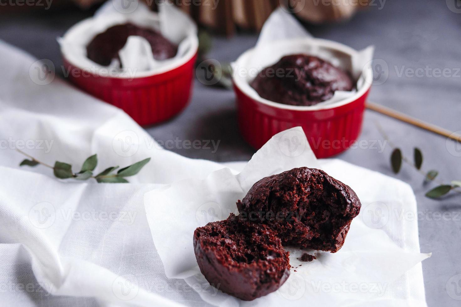 muffins de chocolate em copos vermelhos. pequeno ramekin de cerâmica vitrificada com bolos marrons em um fundo cinza e branco. foto