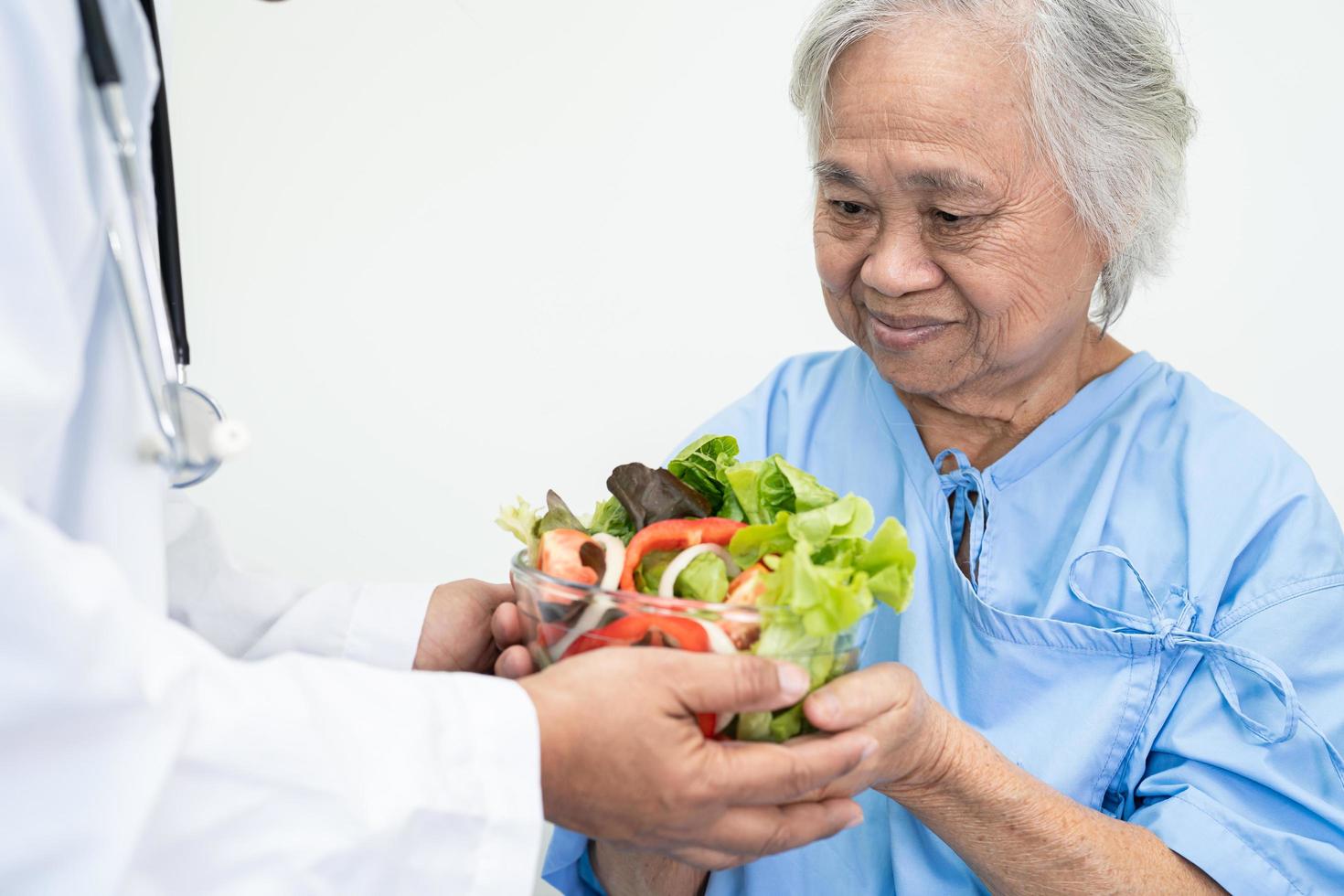 paciente asiático sênior ou idosa idosa comendo alimentos saudáveis de vegetais de café da manhã com esperança e feliz enquanto está sentado e com fome na cama no hospital. foto