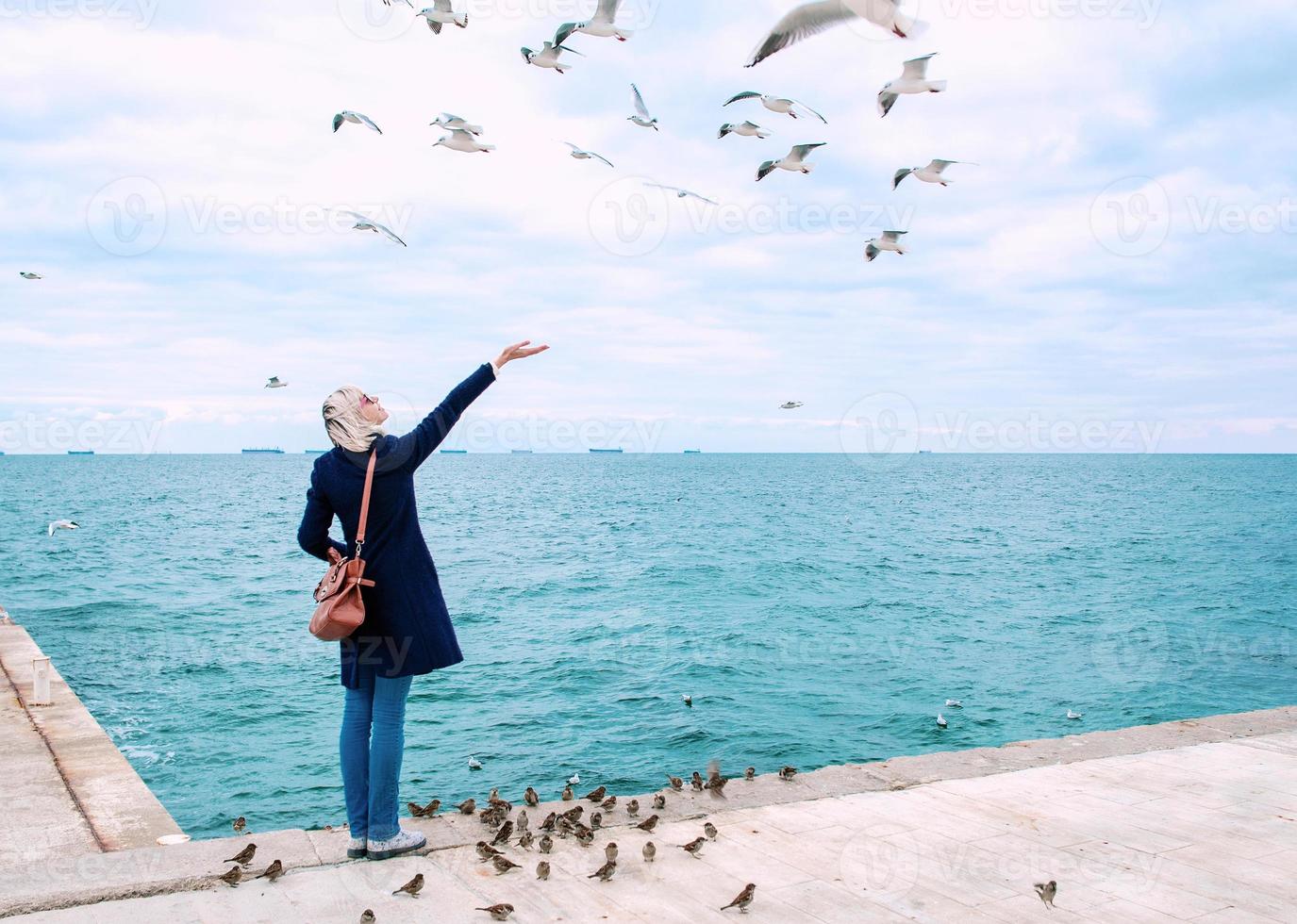 mulher loira alimentando gaivotas em dia nublado de outono na costa do mar foto