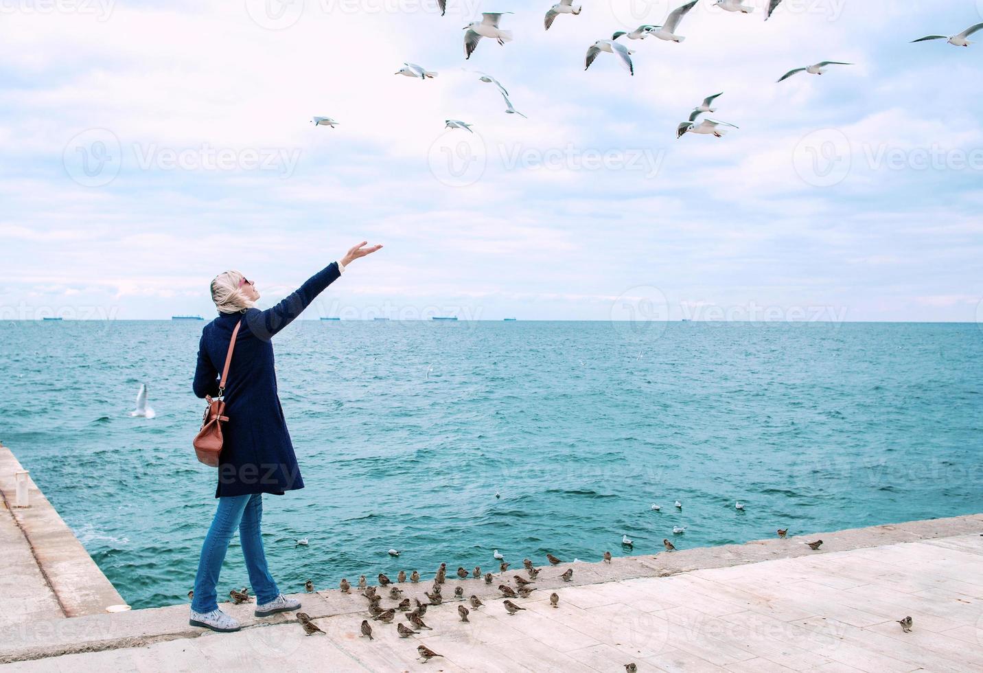 mulher loira alimentando gaivotas em dia nublado de outono na costa do mar foto