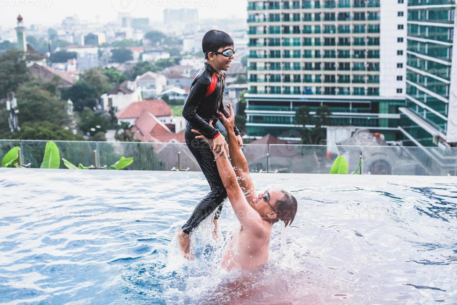 pai pegando seu filho que está pulando na piscina foto