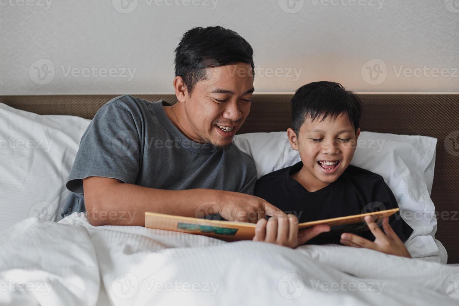 feliz pai e filho lendo um livro juntos na cama foto