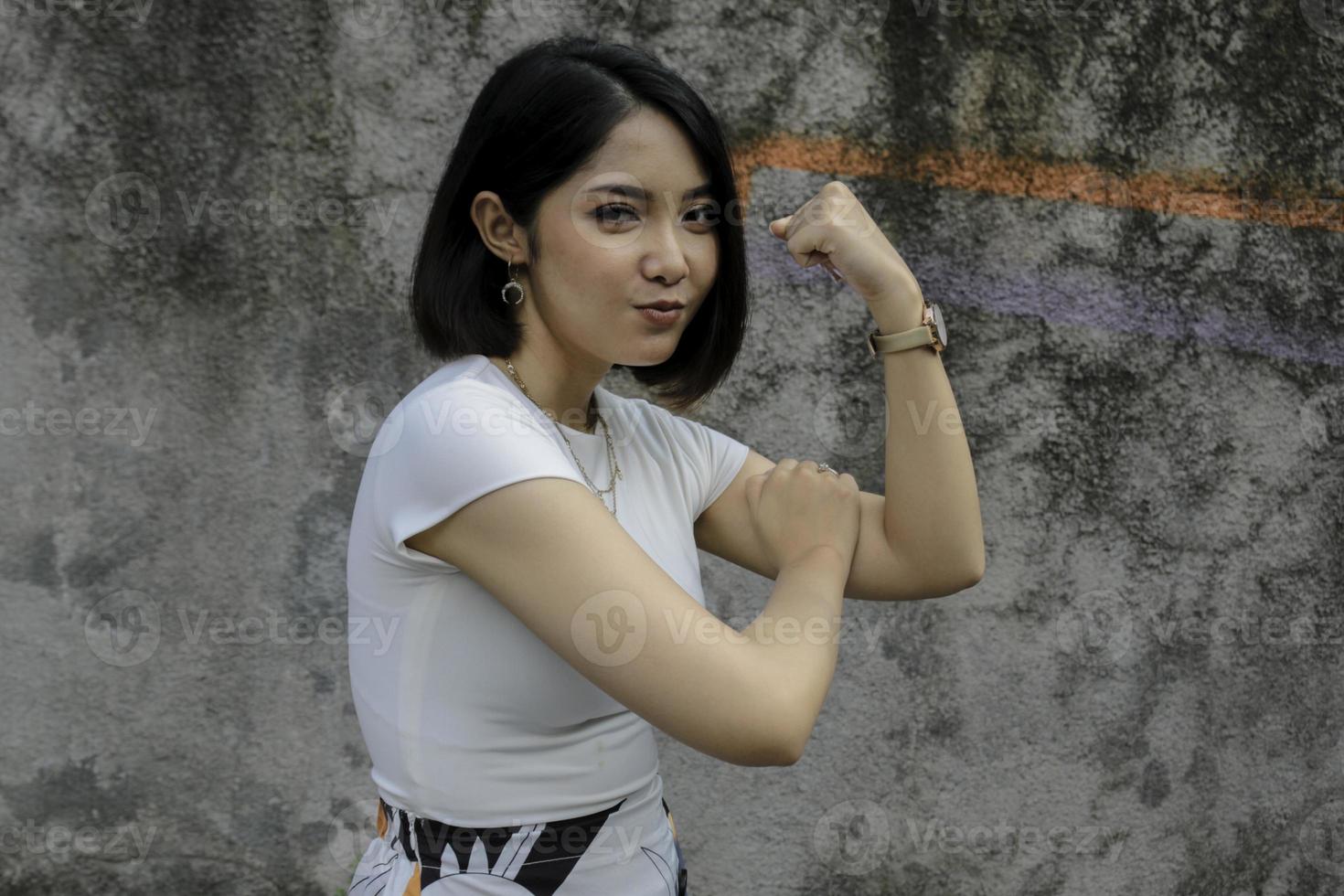 linda jovem asiática forte com camisa branca mostrando bíceps e sorrindo. conceito forte de garota indonésia. foto
