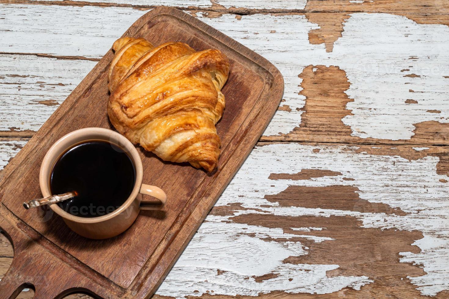 croissant de café da manhã na tábua e café na mesa de madeira branca. foto