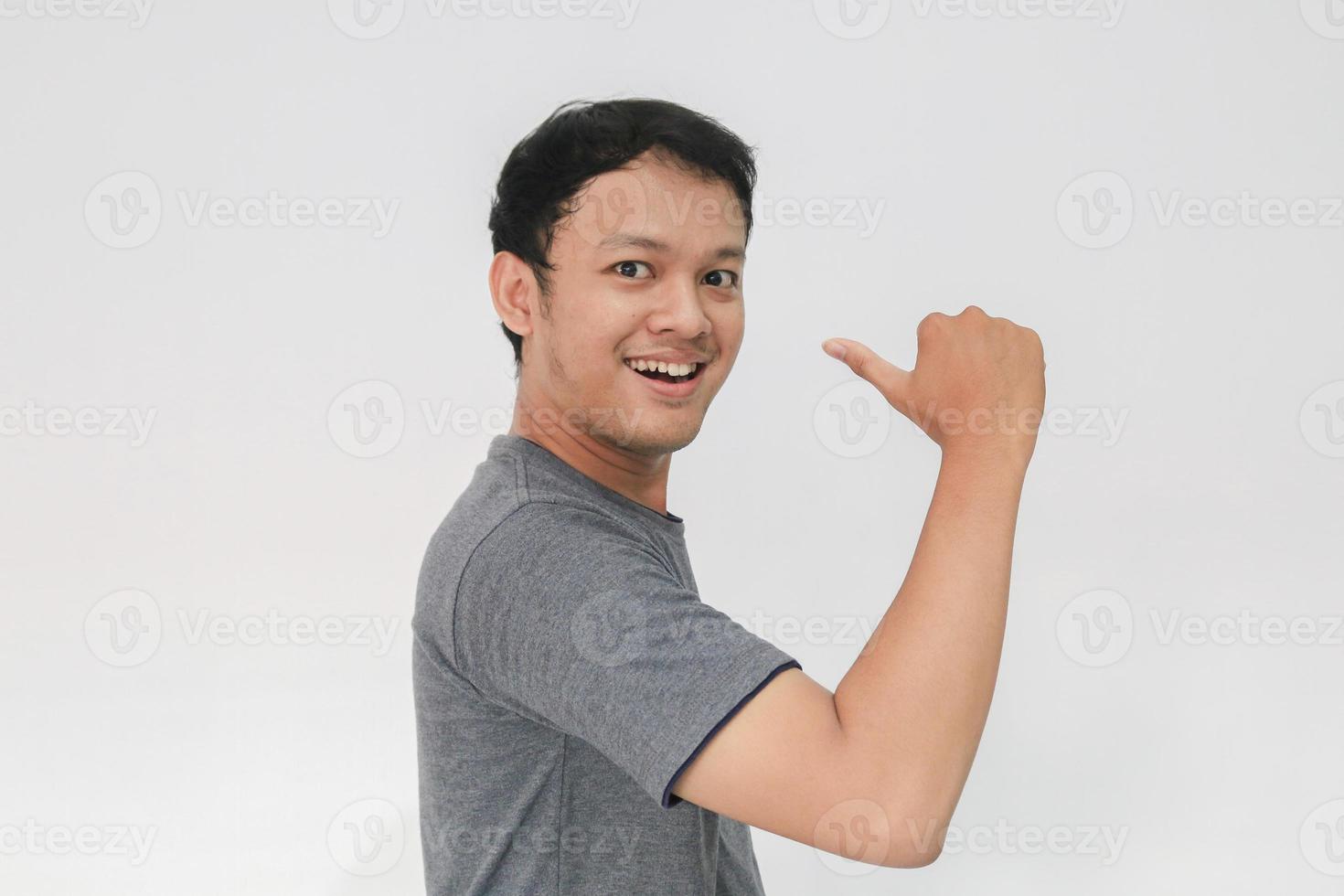 uau e rosto surpreso com sorriso de jovem asiático em camiseta cinza com ponto de mão no espaço vazio. foto