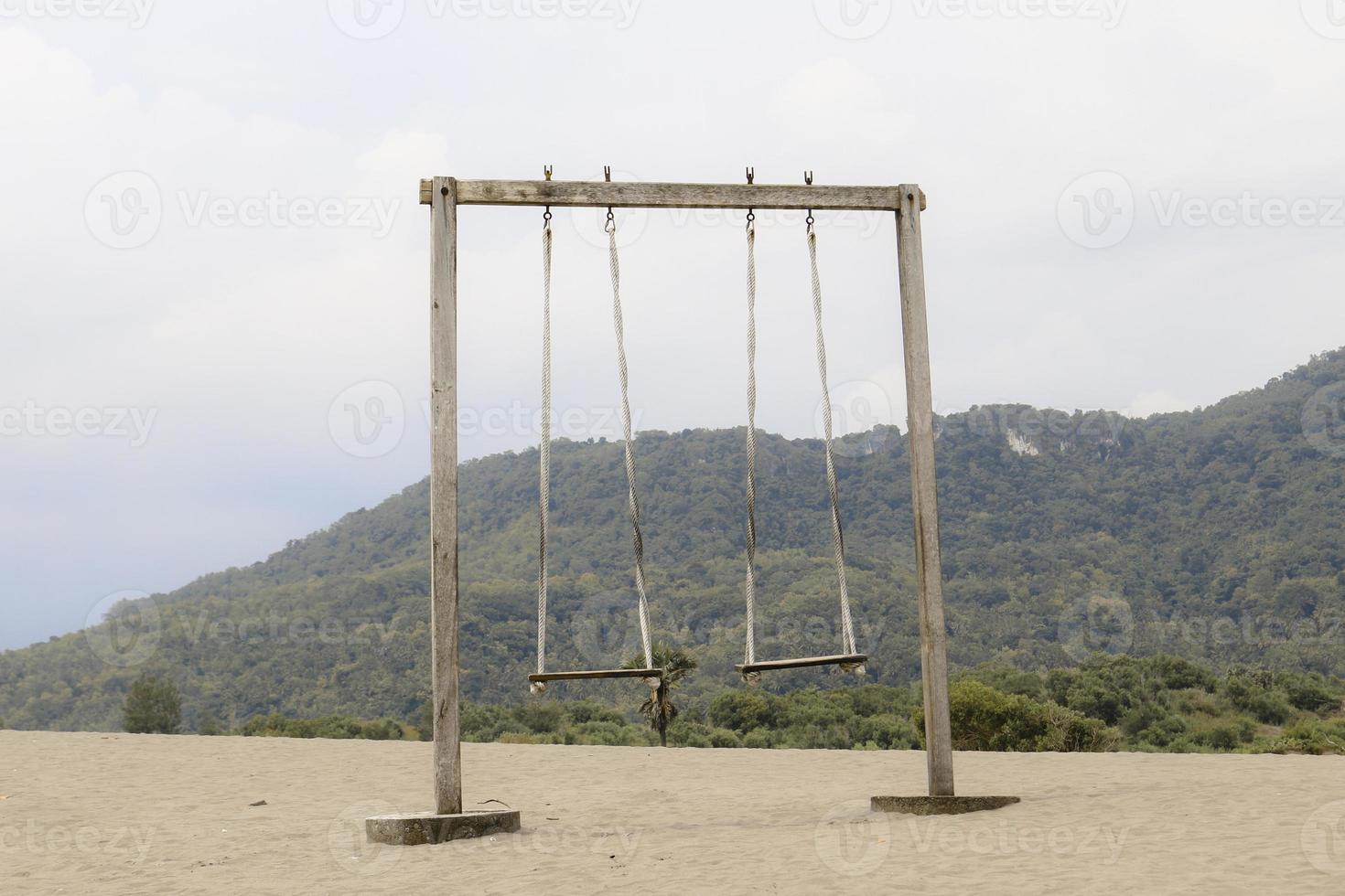 o velho balanço de madeira de corda no deserto ou praia arenosa com fundo de montanha foto