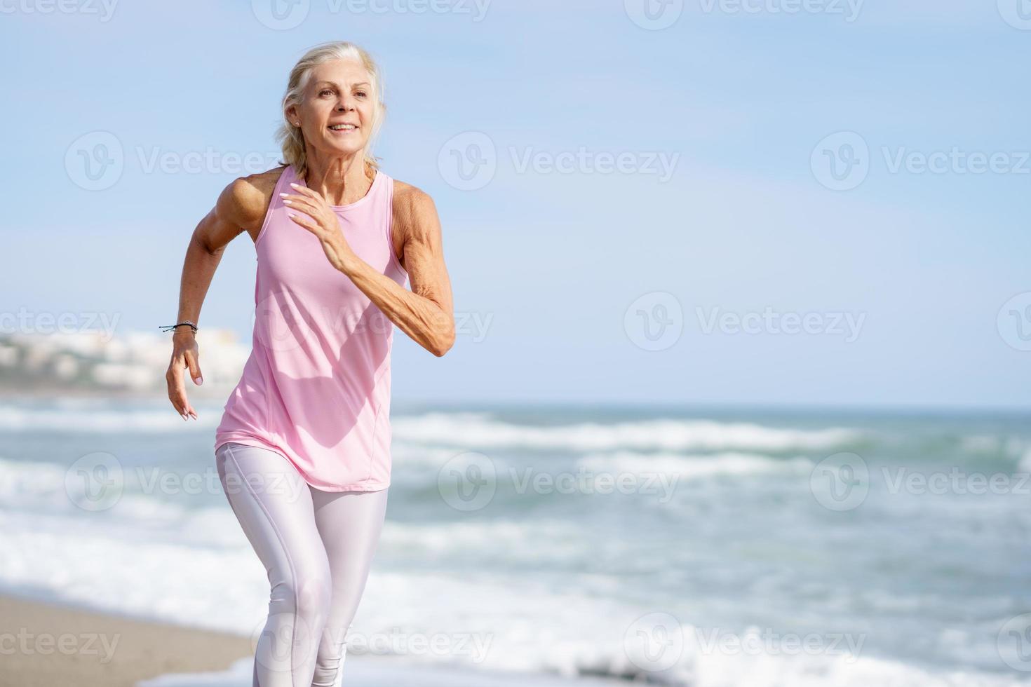 mulher madura correndo ao longo da costa da praia. mulher mais velha fazendo esporte para manter a forma foto