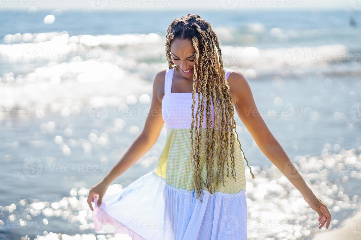 garota negra andando na orla da praia usando um lindo vestido longo. foto