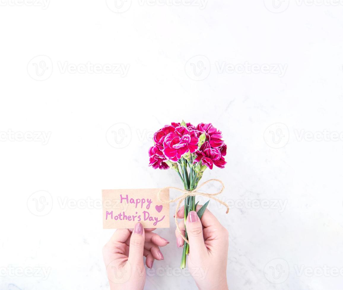 fotografia de conceito de ideia de dia das mães - belos cravos florescendo amarrados por corda kraft arco segurando na mão de uma mulher isolada na mesa moderna brilhante, espaço de cópia, configuração plana, vista superior foto