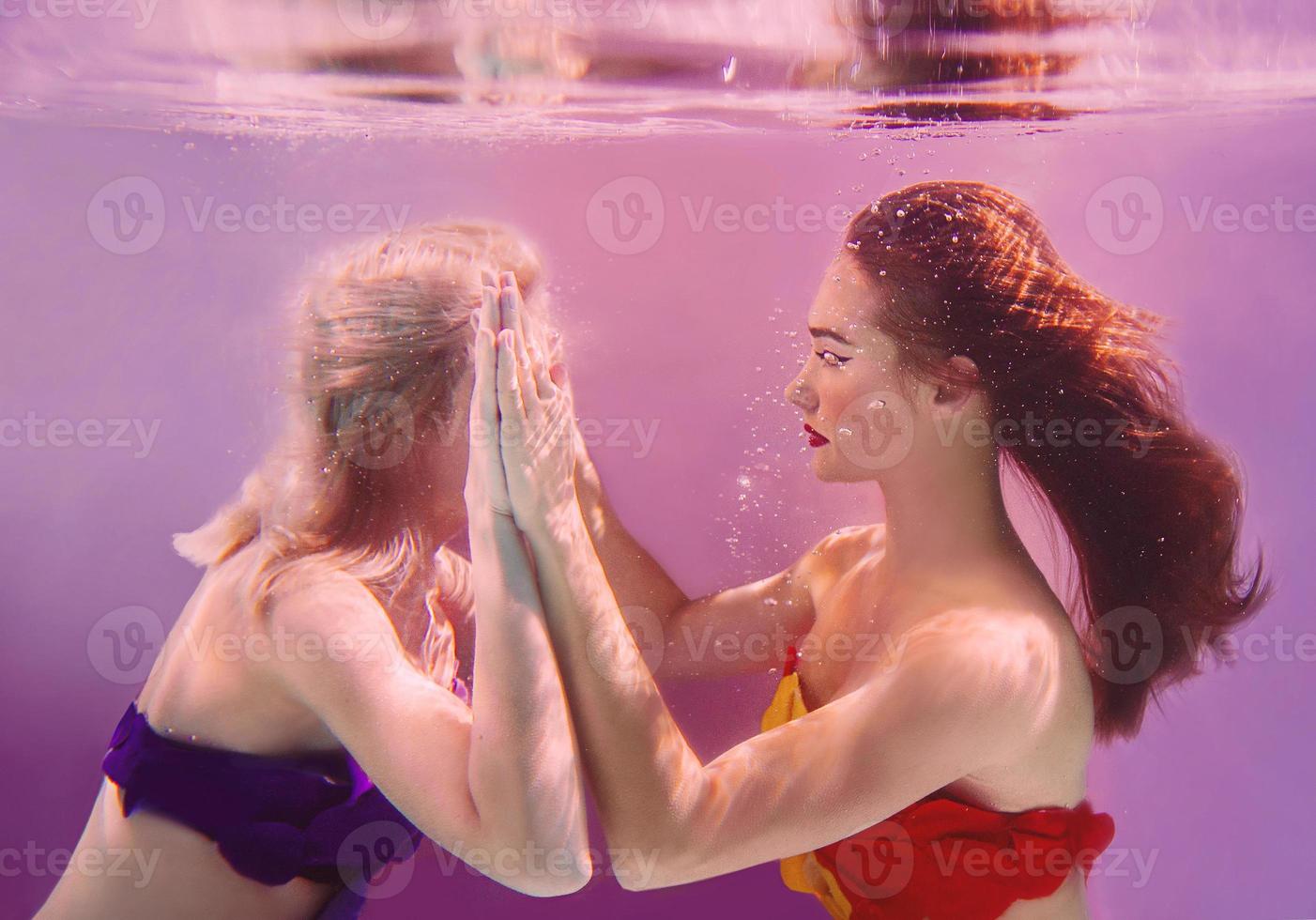 retrato de arte de duas belas mulheres bonitas segurando as mãos debaixo d'água no fundo rosa foto