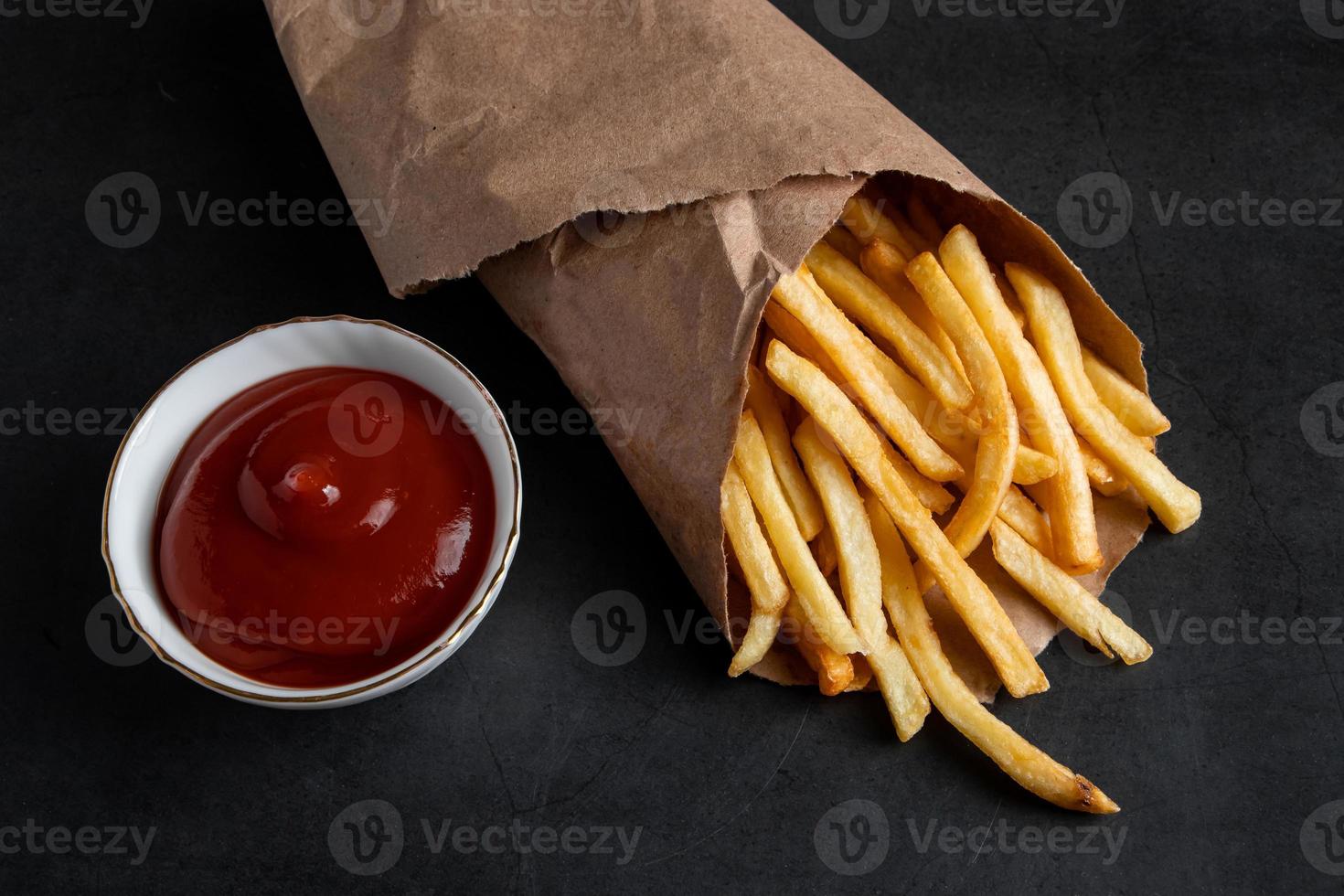 apetitosas batatas fritas crocantes em um saco de papel ecológico em fundo preto. foto