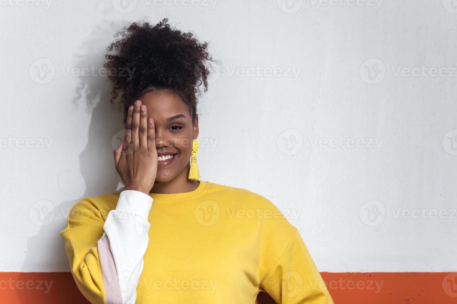 mulher negra sorridente com roupa amarela cobrindo os olhos com a mão foto