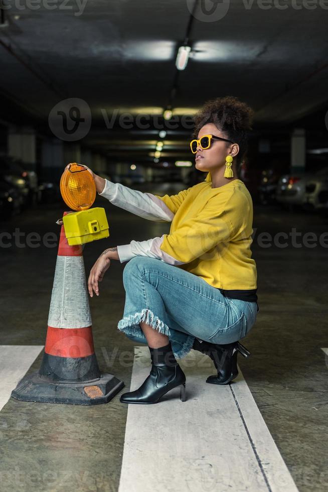 mulher negra na moda hipster de cócoras perto do cone de trânsito foto