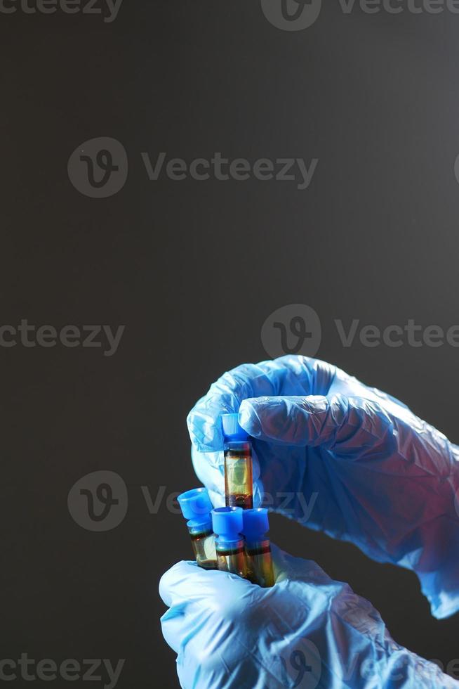 mão em luvas médicas azuis segurando um tubo de teste de sangue foto