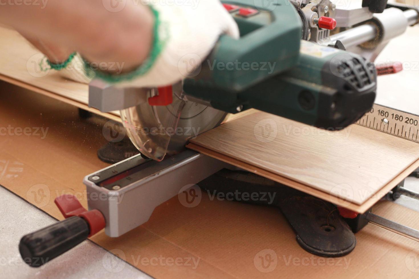 instalação de laminado ou parquet na sala, o trabalhador corta um laminado de um determinado comprimento com uma serra elétrica. auto-reparo do piso da casa foto