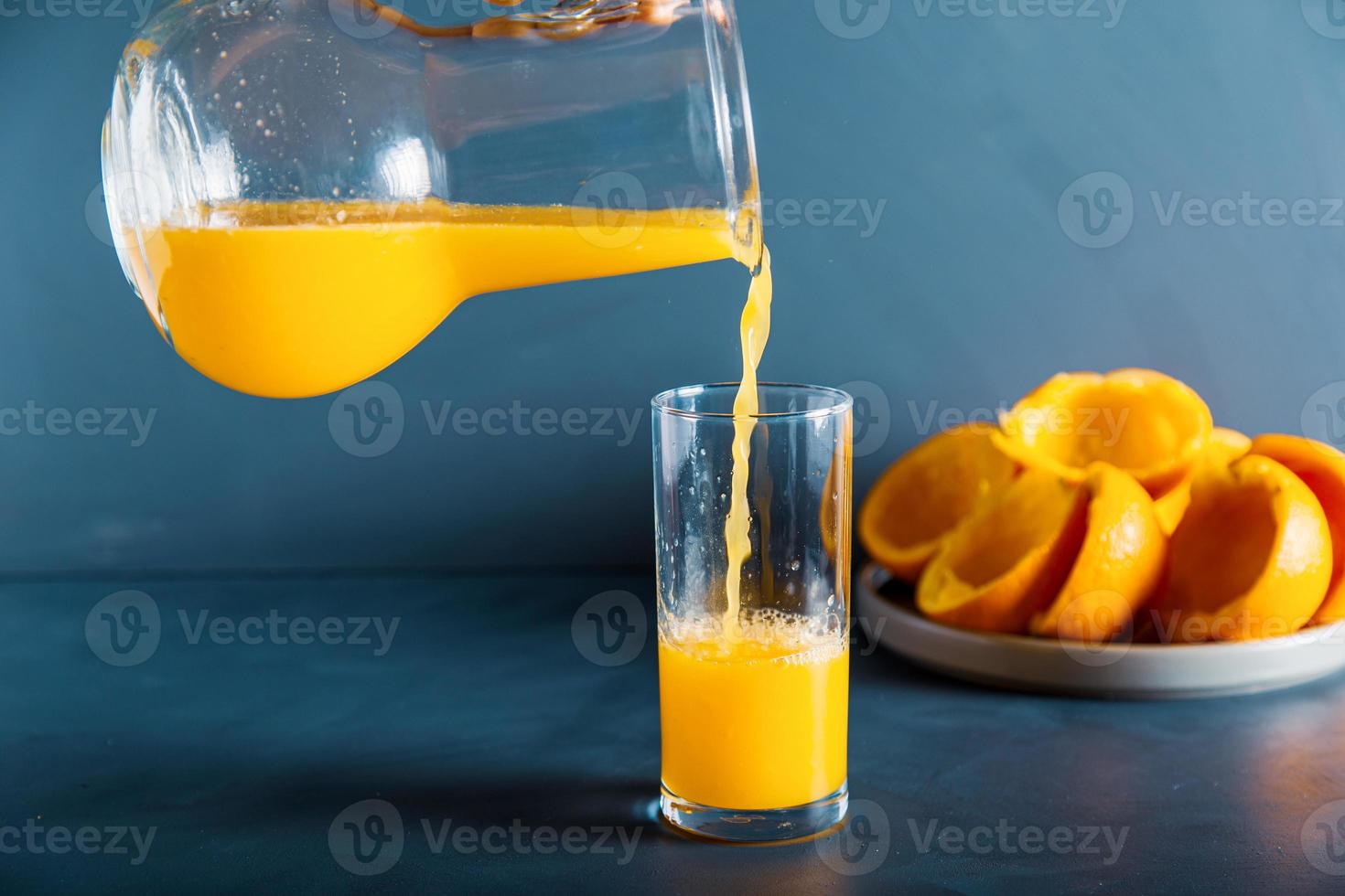 uma mão anônima está enchendo o copo de suco de laranja fresco foto