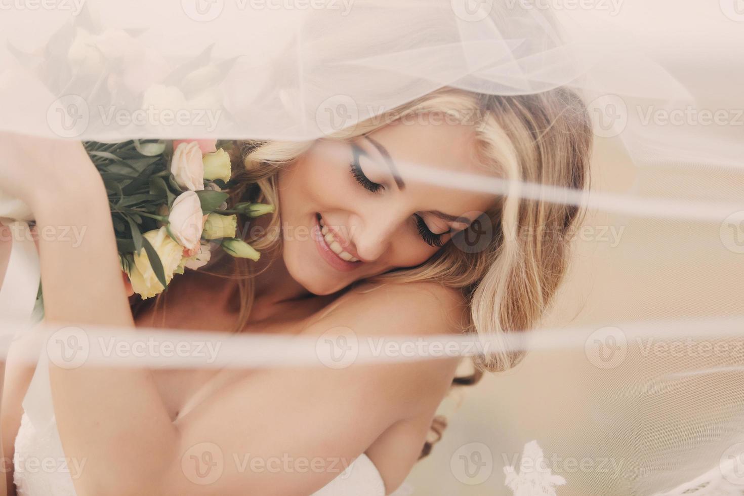 retrato de uma noiva loira linda com um buquê de flores com penteado e maquiagem de casamento. noiva de luxo com véu sobre o rosto. closeup retrato da jovem noiva linda. Casamento. espaço de cópia foto