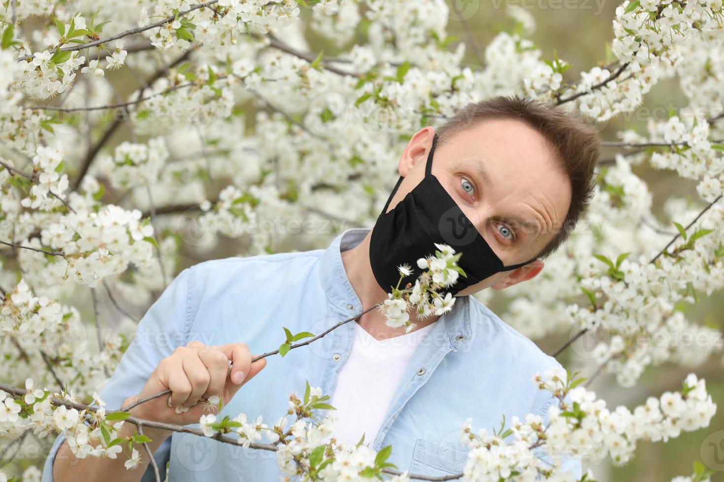 homem mascarado entre árvores floridas. homem com uma máscara médica entre um jardim de primavera florescente. auto-isolamento e quarentena. homem alegre se alegra com o fim da pandemia e aproveita a primavera. foto