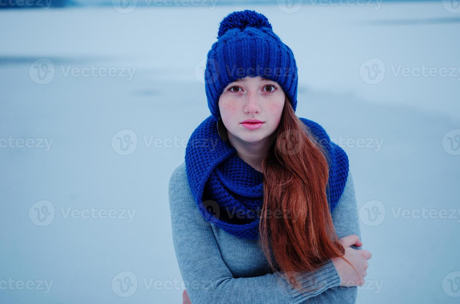 retrato de uma jovem ruiva com sardas vestindo chapéu de lã de malha azul e cachecol no gelo de fundo de dia de inverno. foto