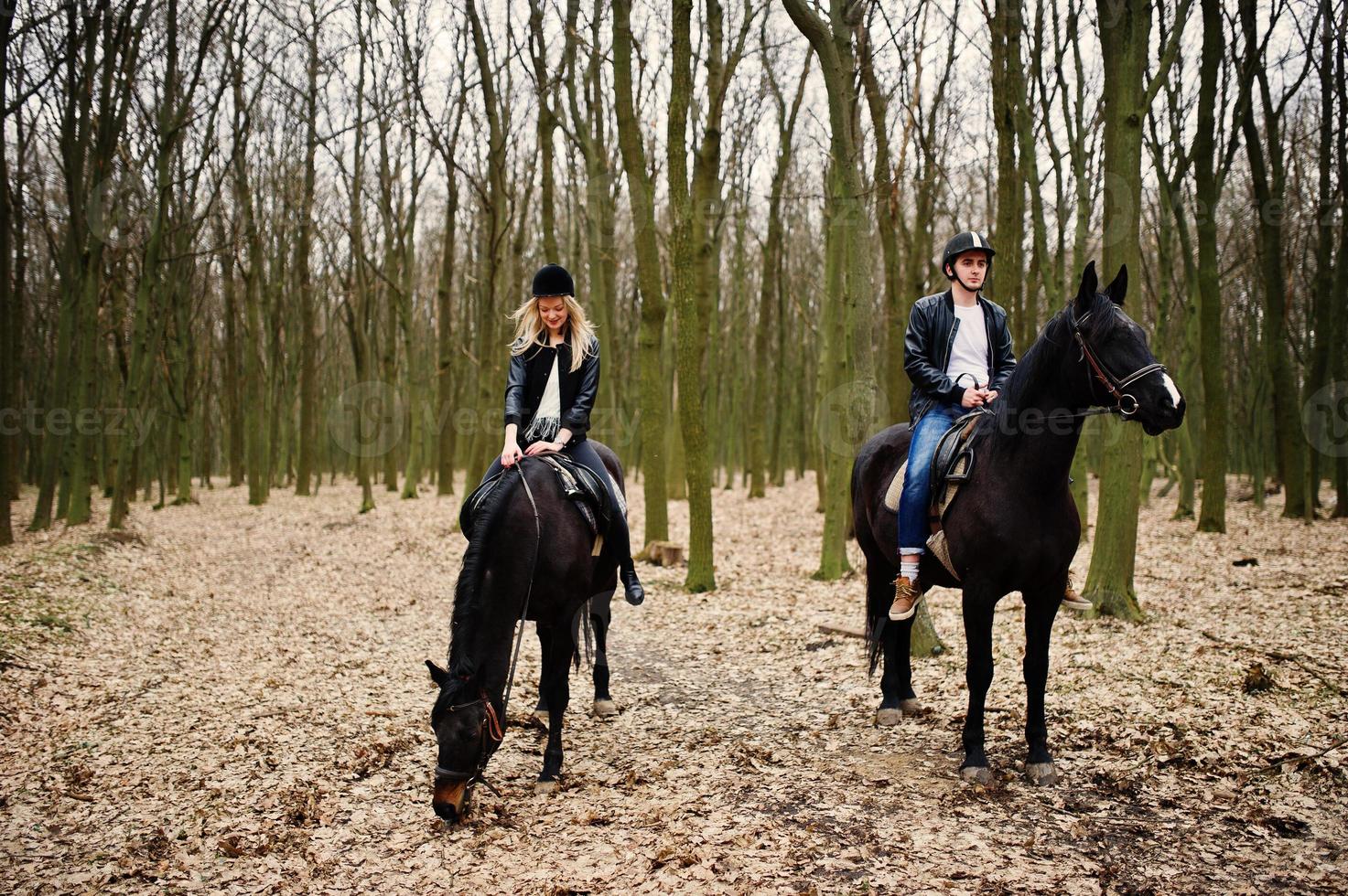 jovem casal elegante montando cavalos na floresta de outono. foto