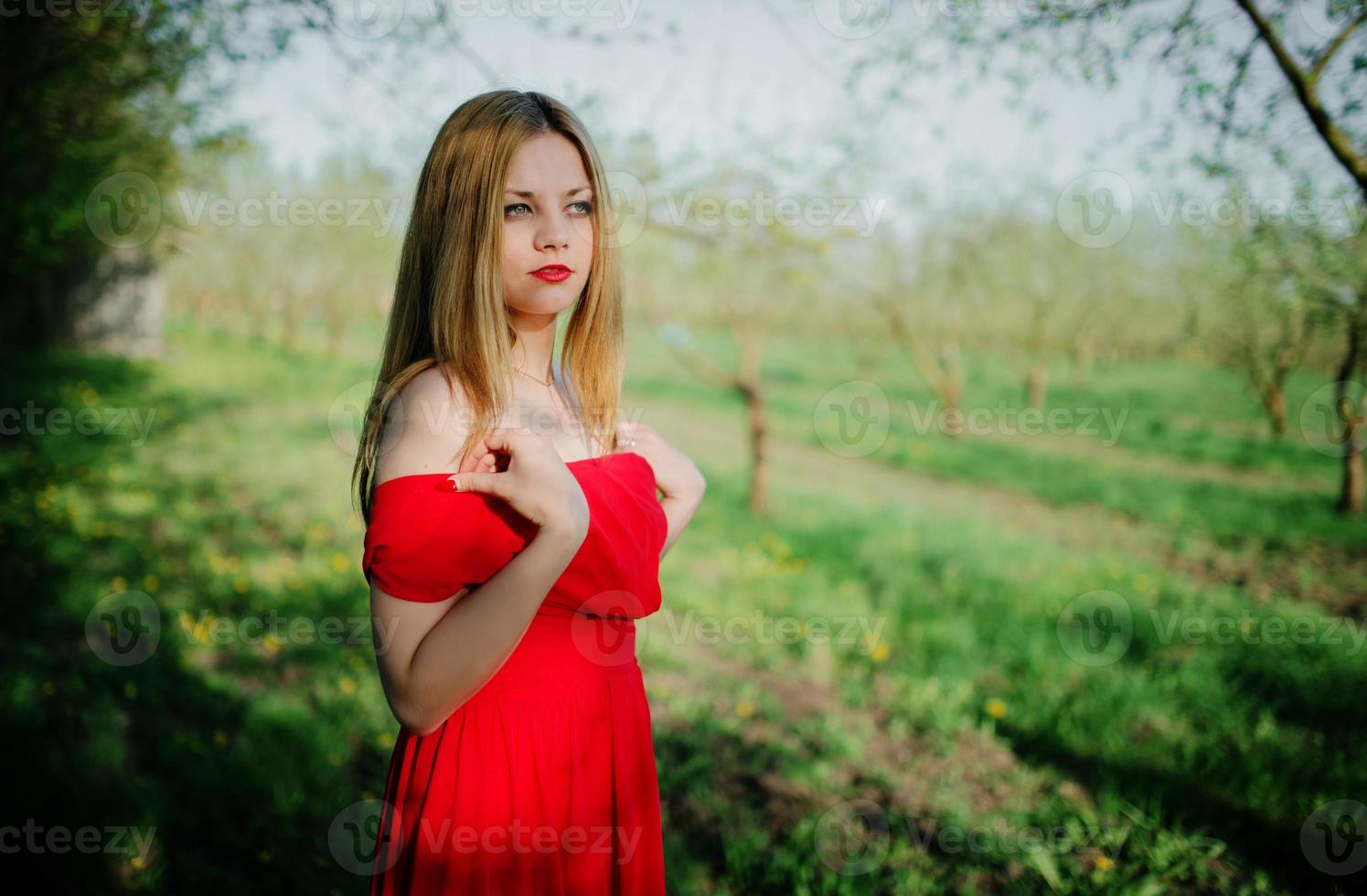 retrato de menina de cabelo claro no jardim de primavera de fundo de vestido vermelho. foto