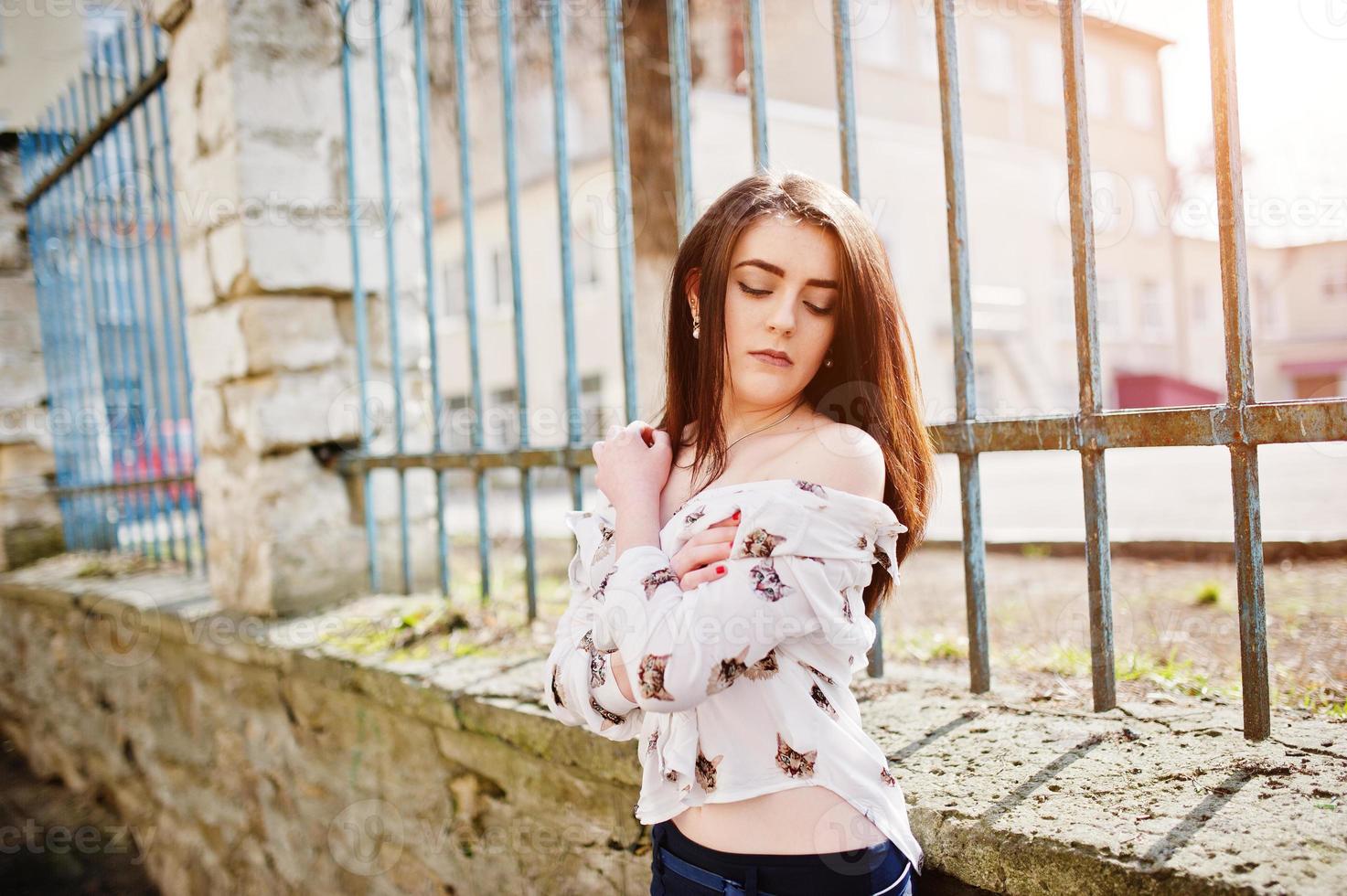 jovem morena elegante na camisa com gatos e calças azuis posou cerca de ferro de fundo. conceito de modelo de moda de rua. foto