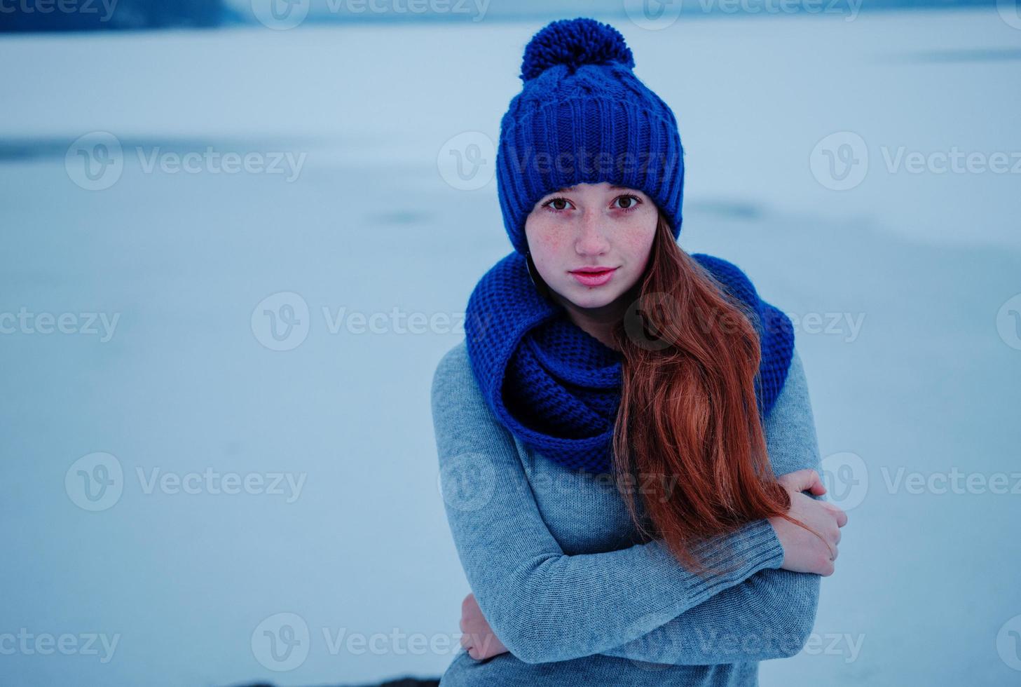 retrato de uma jovem ruiva com sardas vestindo chapéu de lã de malha azul e cachecol no gelo de fundo de dia de inverno. foto