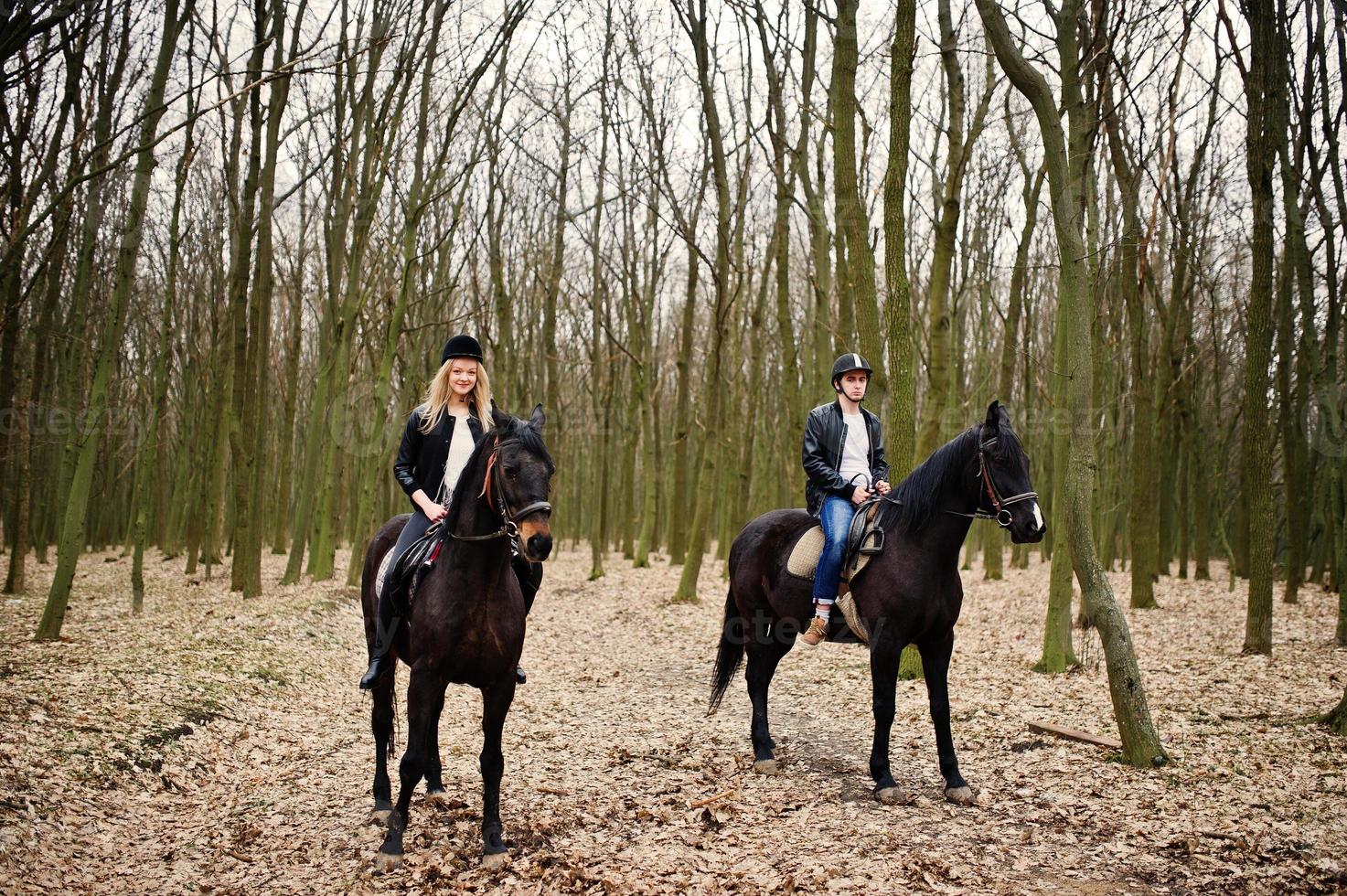 jovem casal elegante montando cavalos na floresta de outono. foto