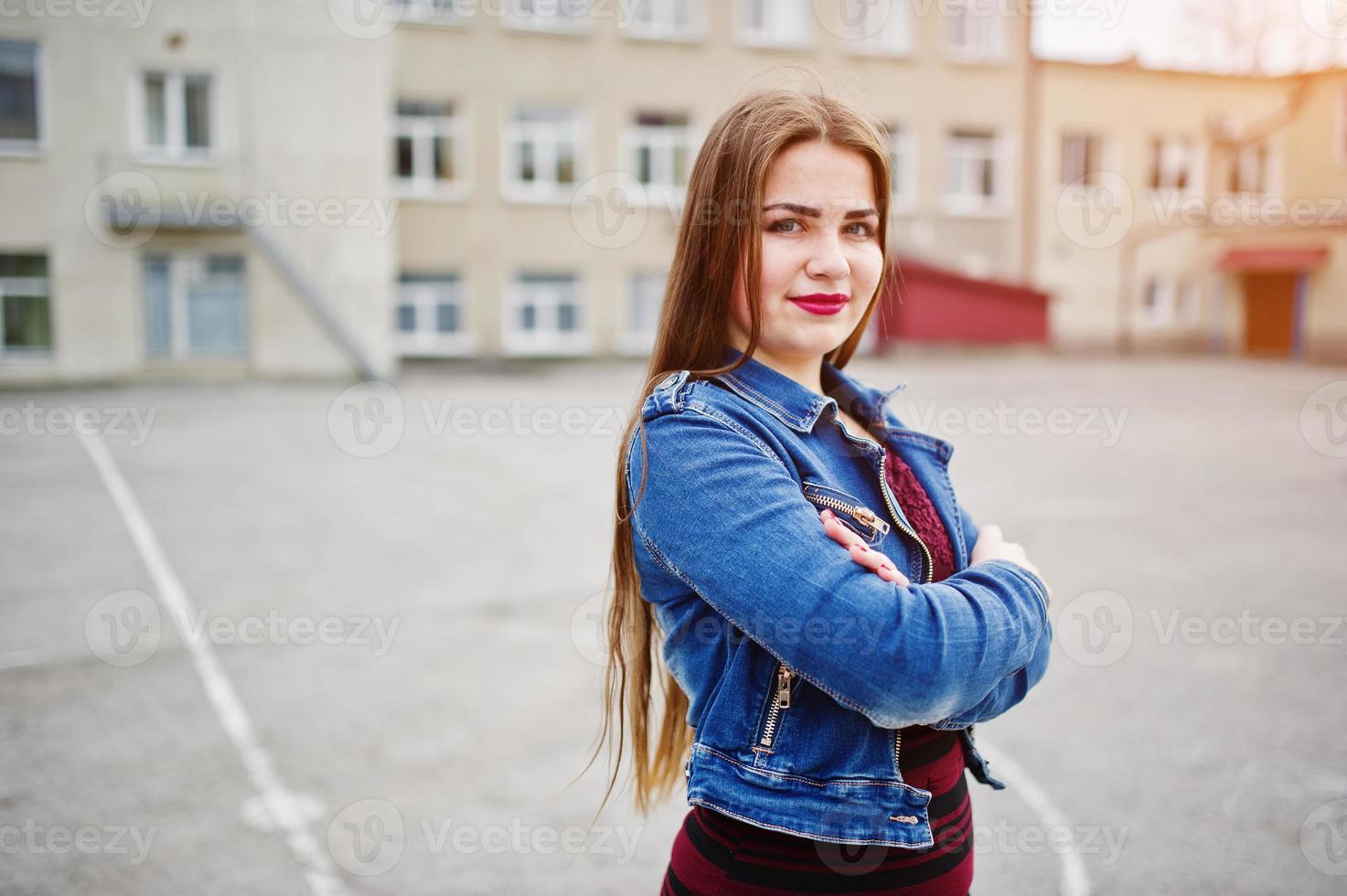 jovem adolescente gordinha usar vestido vermelho e jaqueta jeans posou contra o quintal da escola. foto