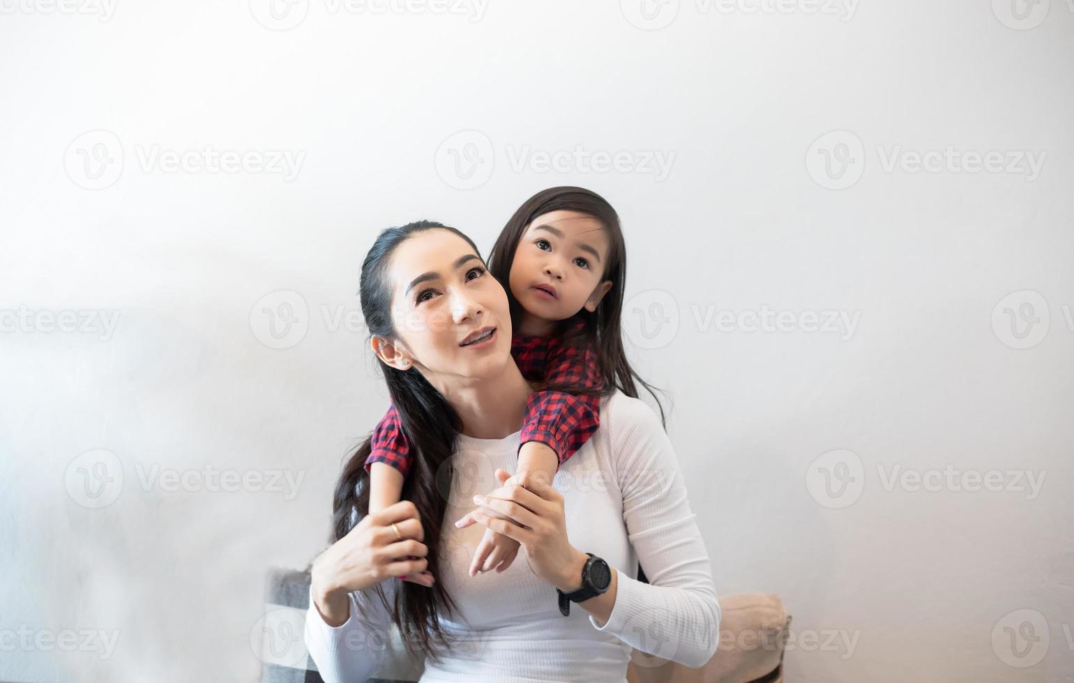 a filha está abraçando e brincando com a mãe e rindo e sorrindo feliz no sofá enquanto relaxa em casa. foto