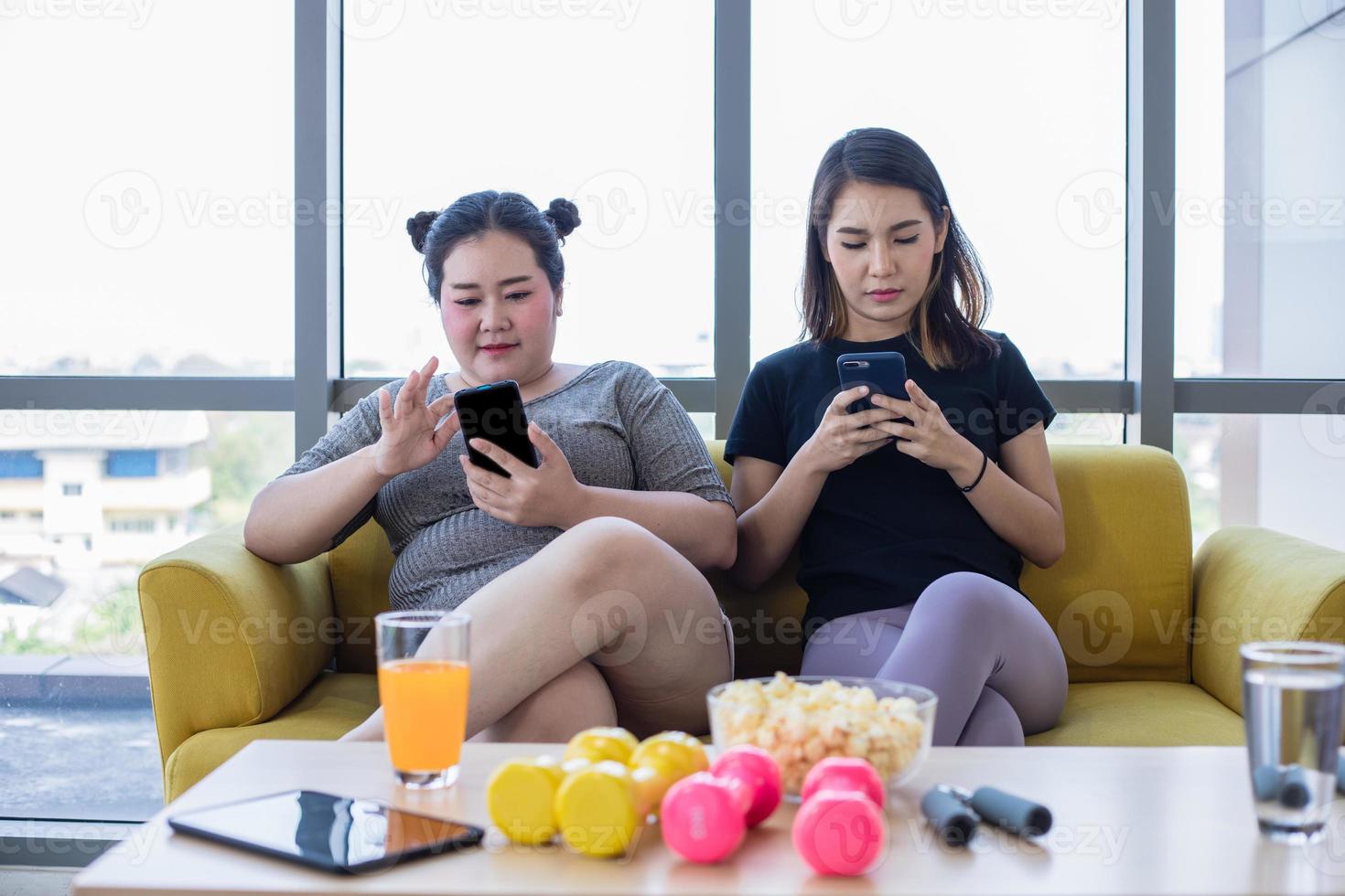 mulher asiática com excesso de peso com amigo joga celular e gosta de comer comida no sofá em casa foto