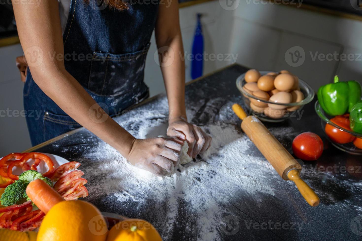 mulheres asiáticas preparando uma pizza, amassar a massa e colocar ingredientes na mesa da cozinha foto