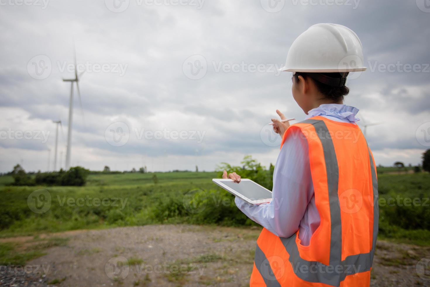 Engenheiro asiático com capacete de segurança usando computador tablet pc, inspecionando e trabalhando na estação geradora de energia de uma fazenda de turbina eólica foto