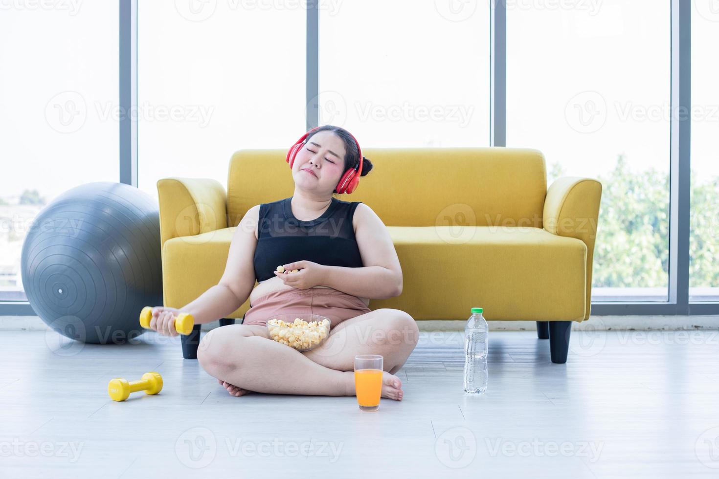 mulher asiática com excesso de peso usando tablet e. usando fone de ouvido para ouvir música e ela está se exercitando em casa, menina asiática gosta de comer comida e pipoca foto